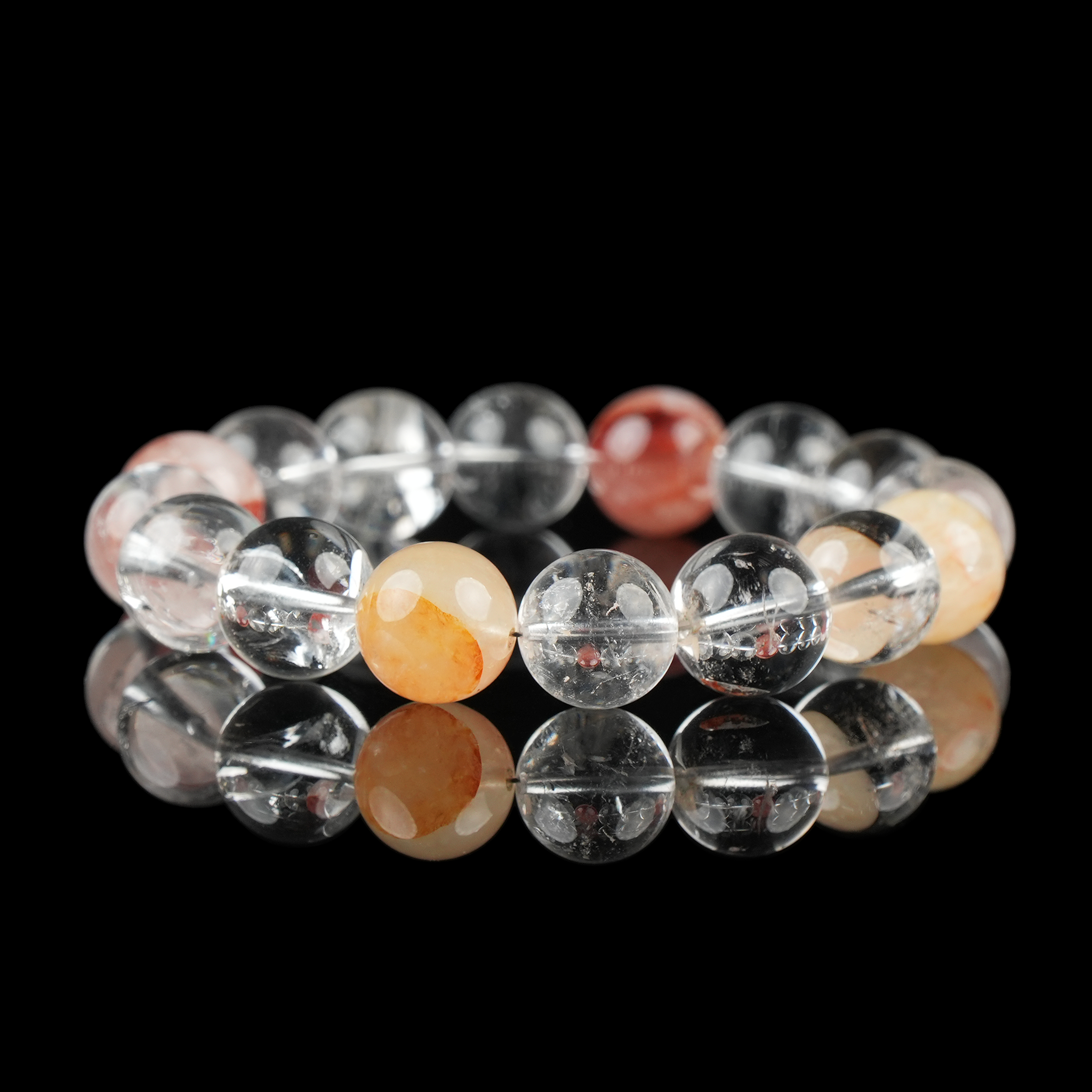 A crystal bracelet featuring translucent Clear Quartz and vibrant Hematoid Quartz beads, arranged in a circular pattern and shown on a glossy black background.