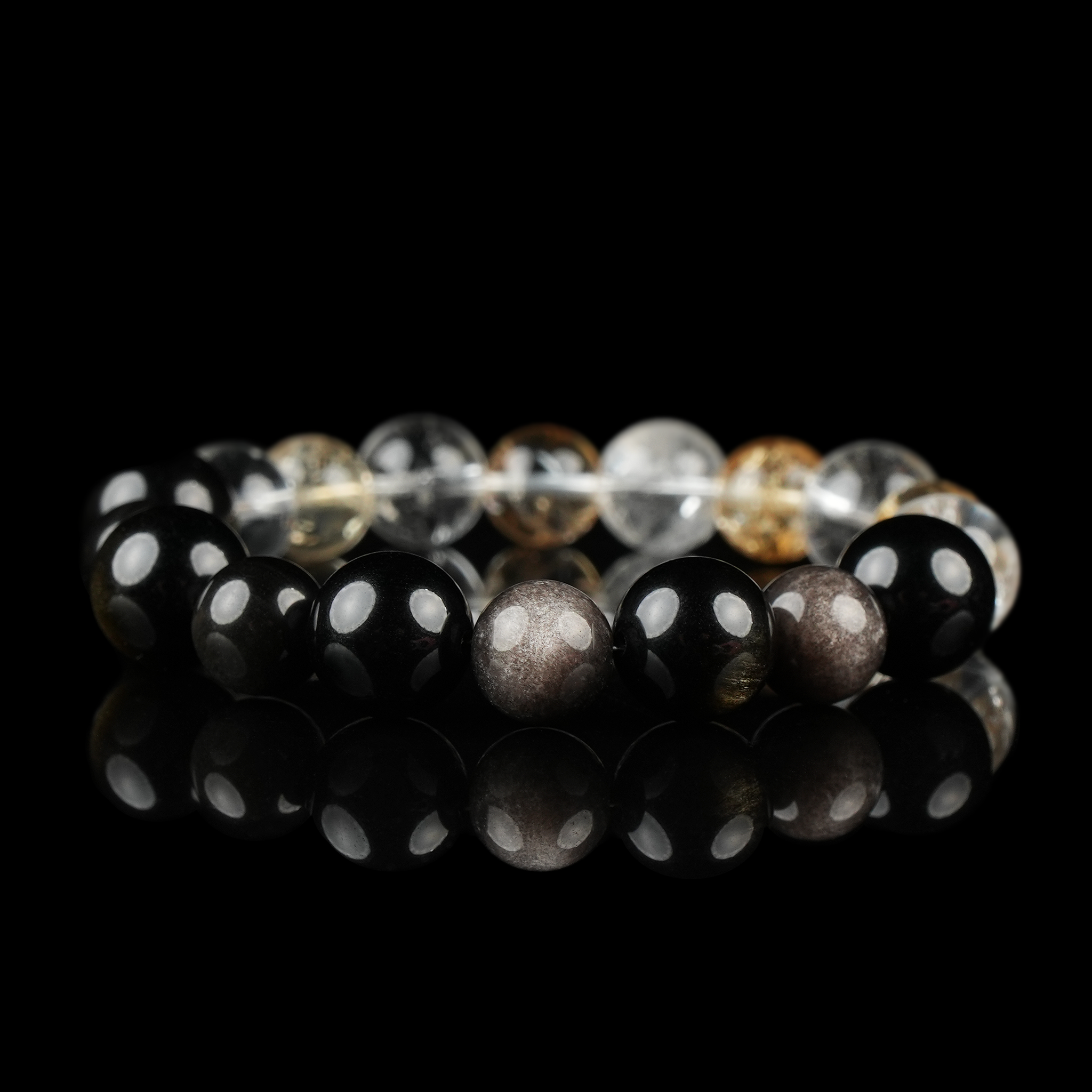 This image shows a polished bracelet composed of glossy 12mm beads, including transparent Clear Quartz, golden-hued Citrine, deep black Obsidian, and shimmery Silver Obsidian. The bracelet is displayed against a black reflective background, enhancing the brilliance and contrast of each stone’s natural color and texture.