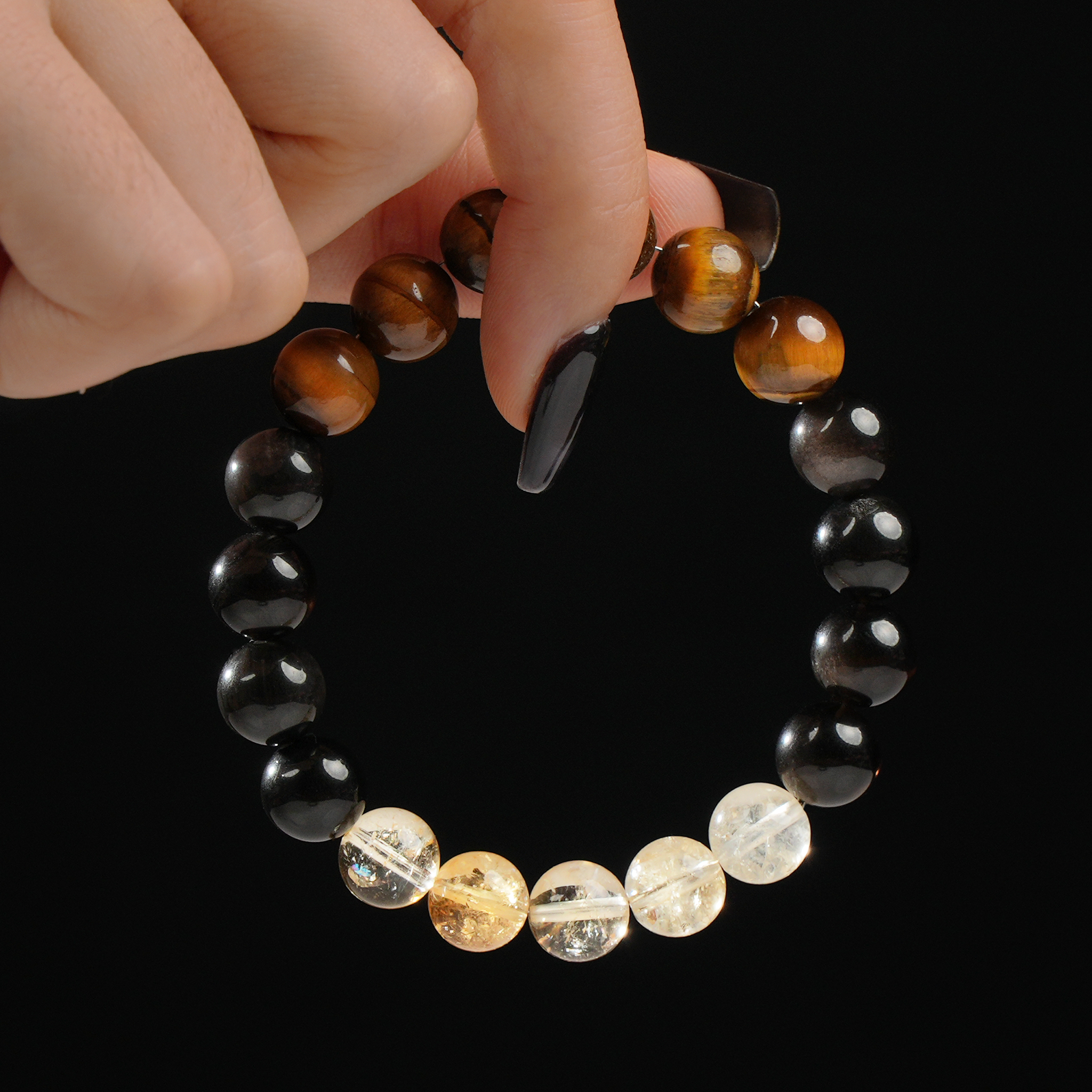A person gently holds a gemstone bracelet composed of 12mm beads, showcasing the radiant blend of Tiger’s Eye, luminous Citrine, and reflective Silver Sheen Obsidian stones.