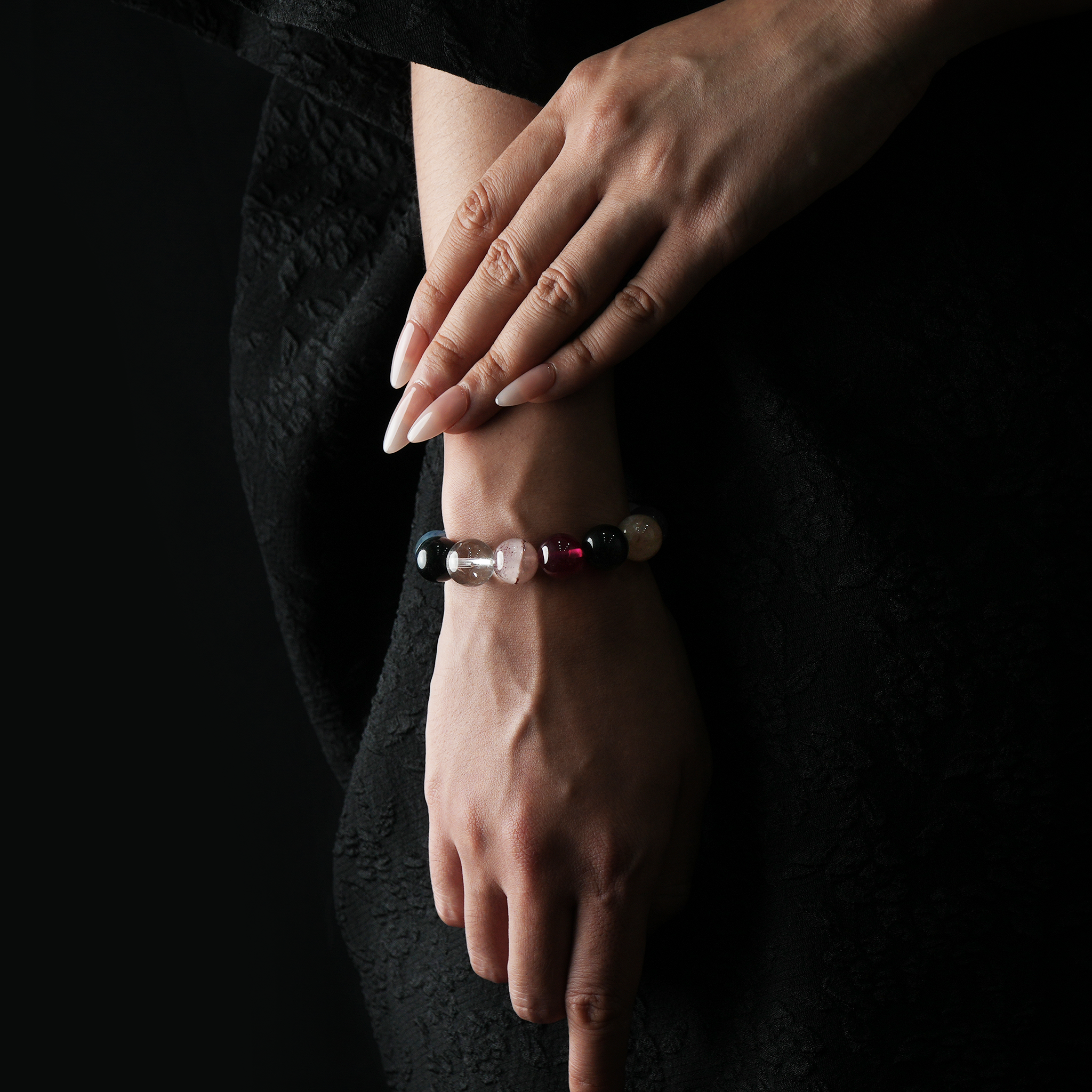A woman wearing a multistone crystal bracelet featuring amethyst, rose quartz, tiger’s eye, red rutilated quartz, chalcedony, citrine, snow phantom, moonstone, aquamarine, clear quartz, strawberry quartz, garnet, and flower agate.