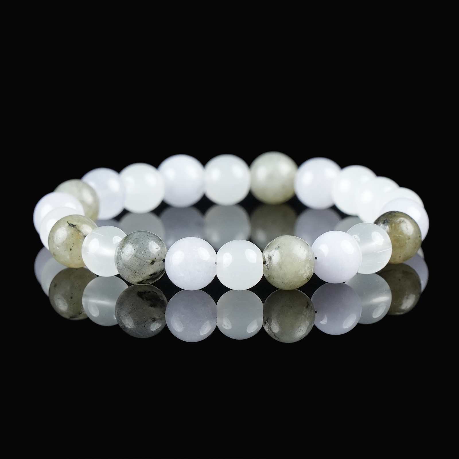 Close-up of a bracelet made with moonstone, aquamarine, and quartz beads, displayed on a glossy black surface to highlight its soft glow and serene energy.