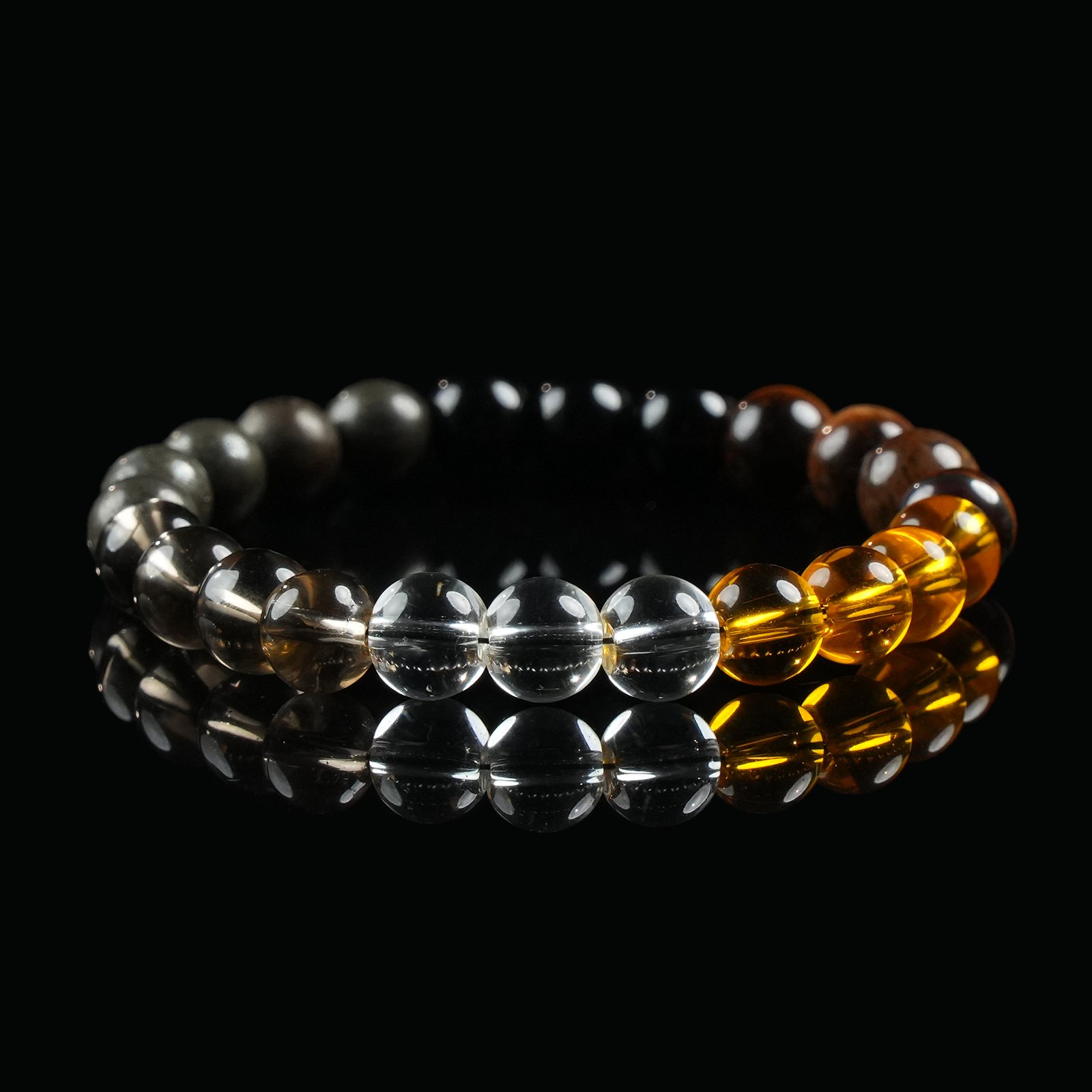A close-up of a bracelet composed of black obsidian, golden tiger’s eye, smoky quartz, and clear quartz beads, laid flat on a reflective black surface to highlight the vibrant color transitions and energy of each stone.