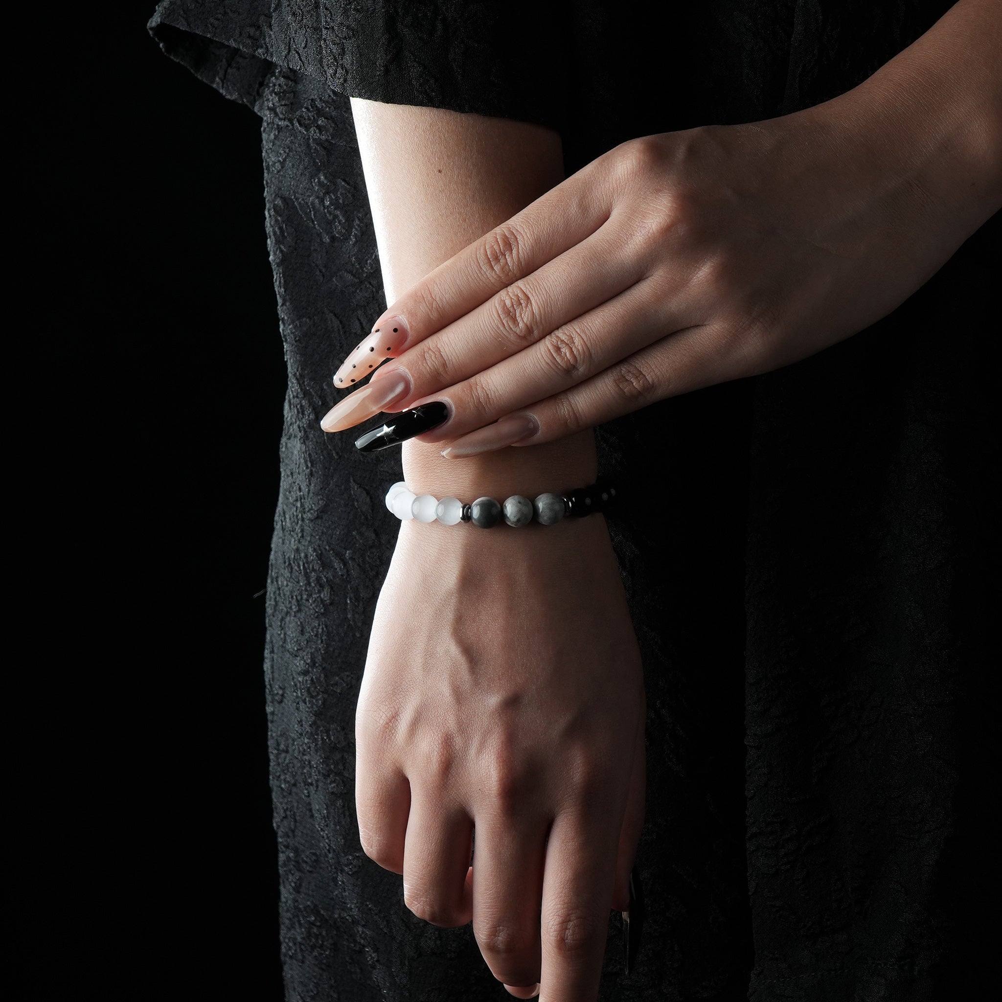 A minimalist bracelet featuring black obsidian and white cat’s eye beads, worn on the wrist with a black lace dress.