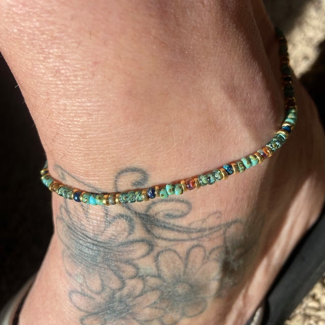 A turquoise crystal anklet worn on an ankle with a tattoo, showing casual beach-style vibes.