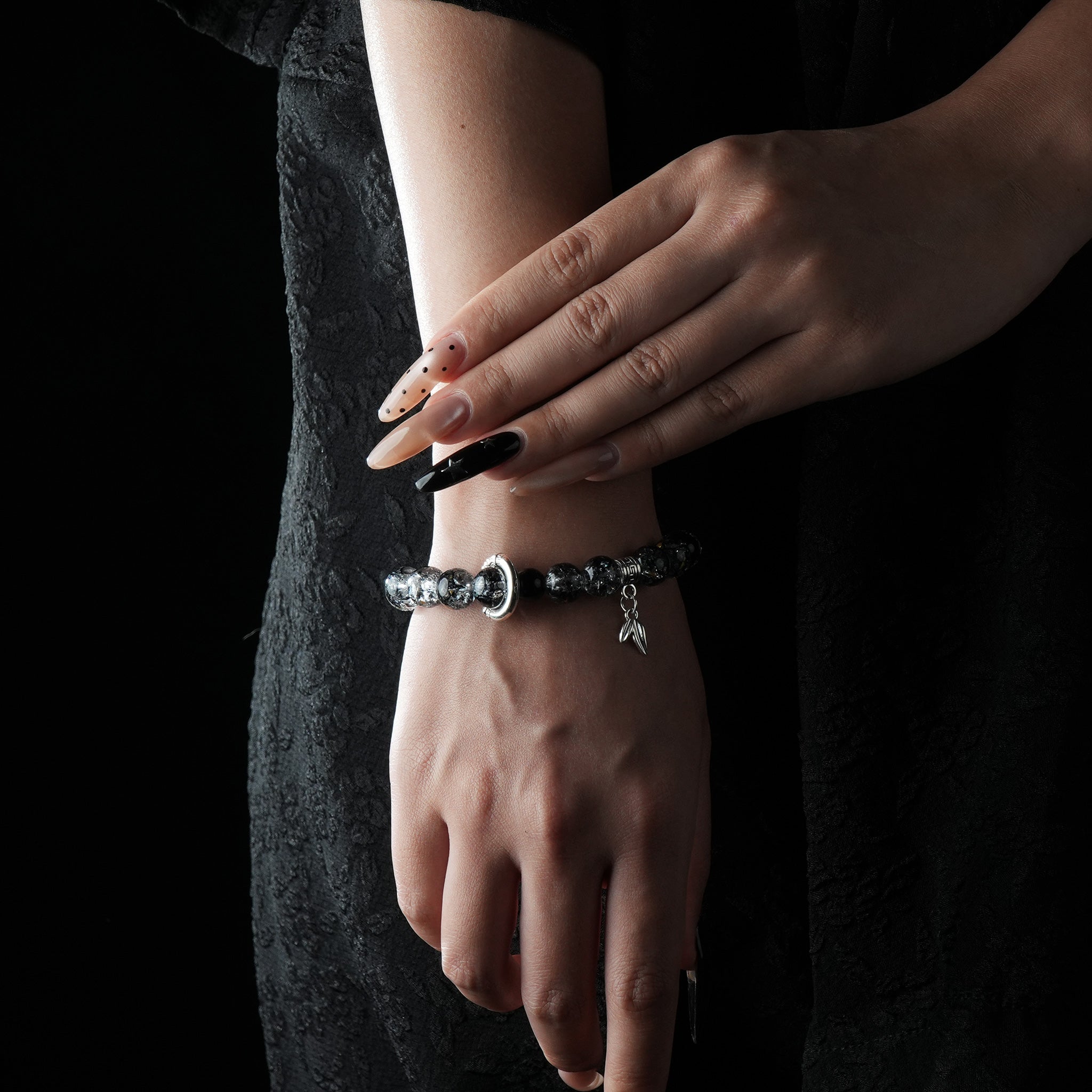 A bracelet featuring celestial energy beads with a moon and feather charm, worn on a wrist against a black outfit.