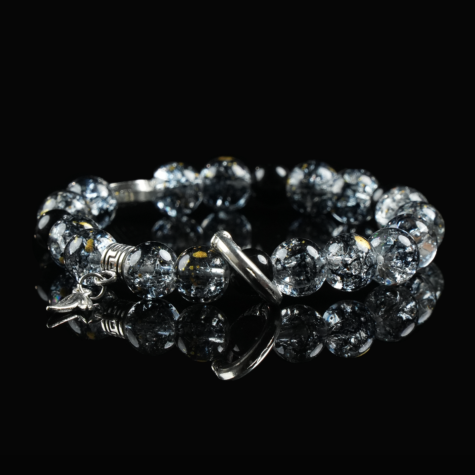 Black rutilated quartz bracelet with celestial-themed silver charms and hook clasp, displayed on reflective surface for spiritual protection.