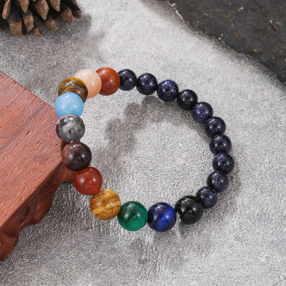 A round beaded bracelet with multicolor planets laid on a wooden display, photographed from an angle.