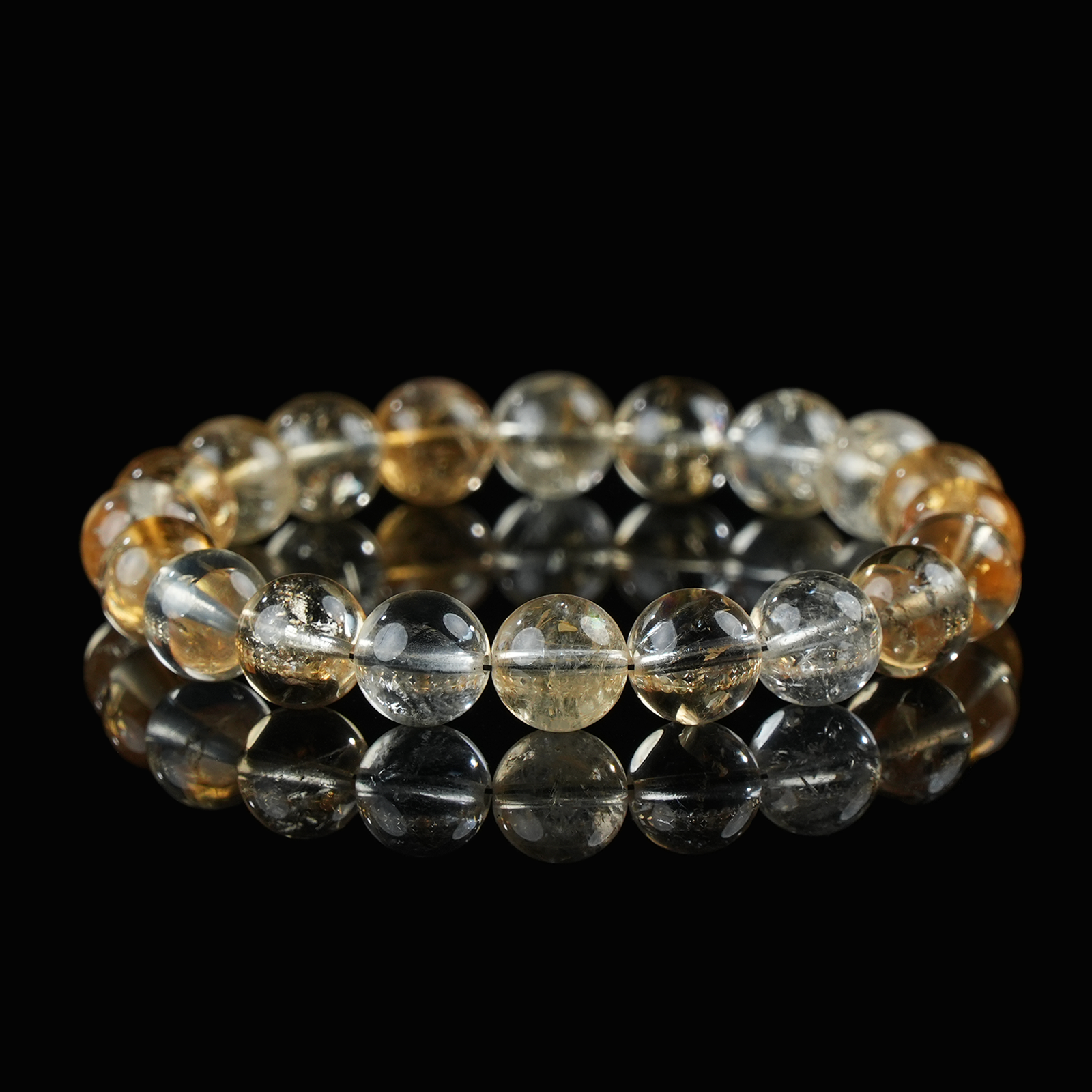 Close-up of a citrine bracelet composed of golden-yellow and clear translucent beads, arranged on a reflective black surface to highlight its radiant clarity and energetic glow.