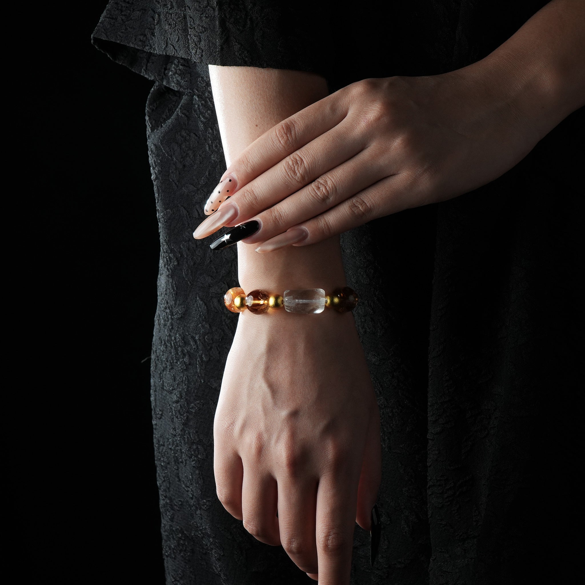 A bracelet featuring citrine crystal, white quartz, and gold-tone beads, worn on the wrist with a black dress.