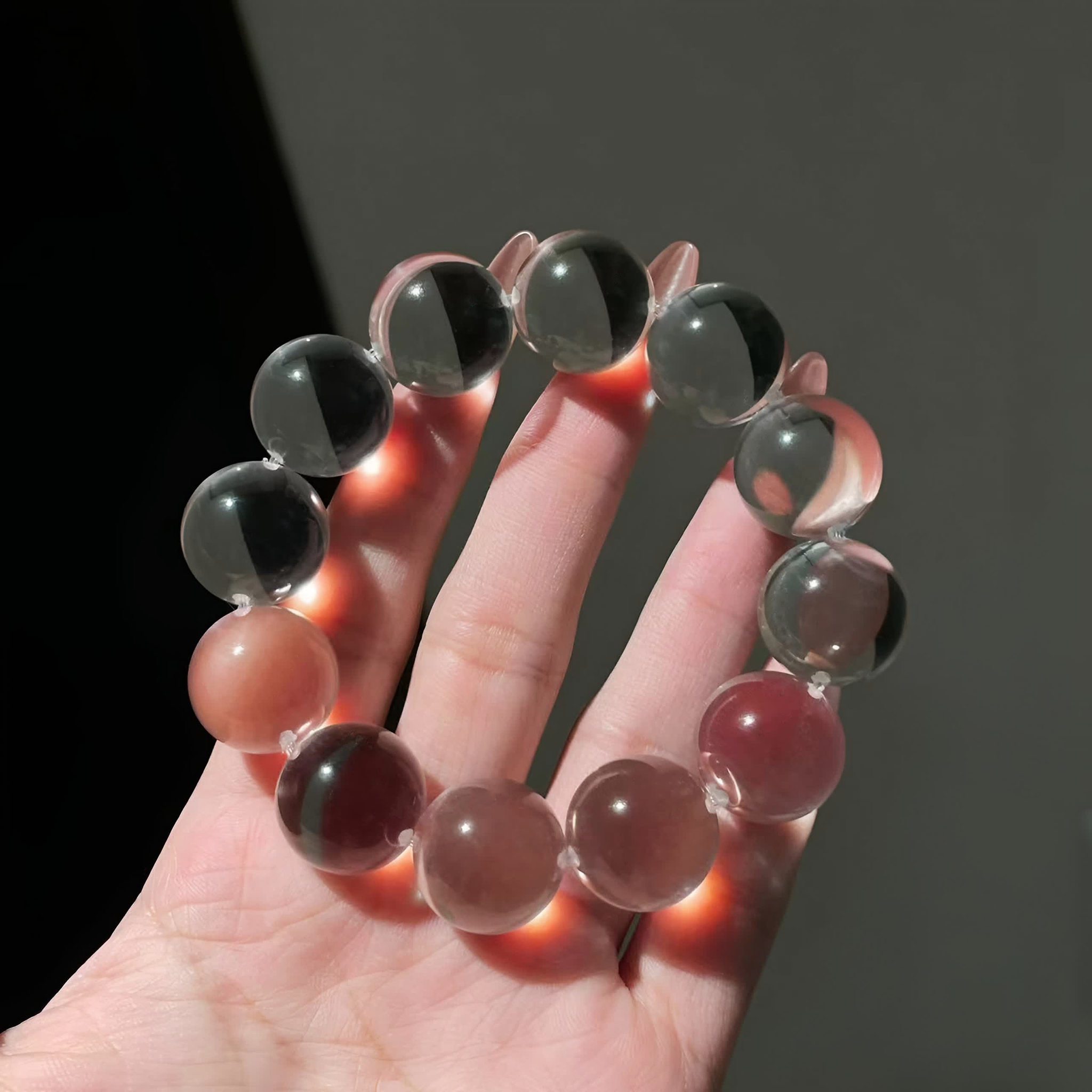 A hand holding a clear quartz crystal bracelet, warm sunlight illuminating the transparent beads.
