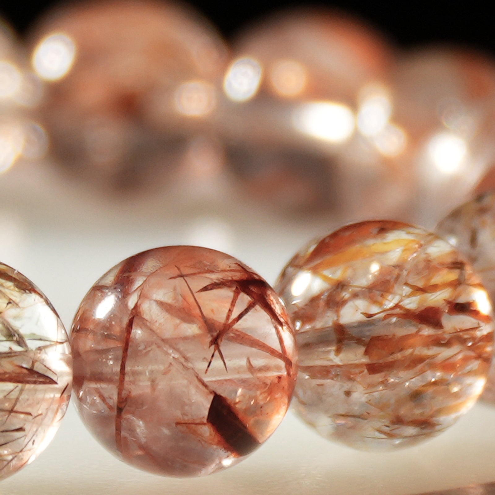 Macro shot of red rutilated quartz crystal beads showing internal needle-like rutile structures and polished surfaces.