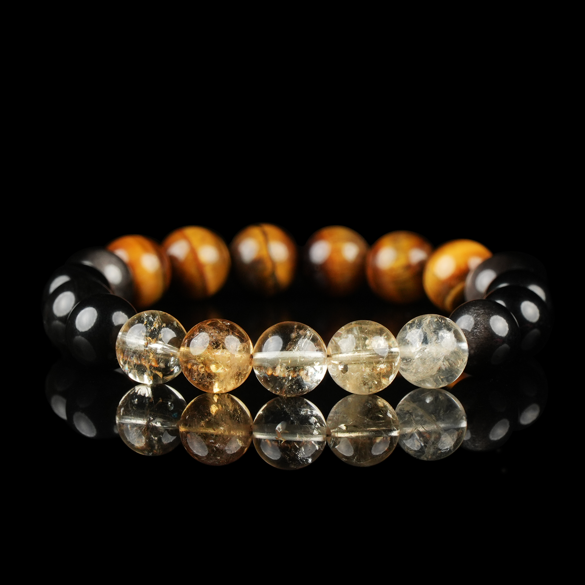 A vivid bracelet combining warm brown Tiger’s Eye, golden-yellow Citrine, and glossy dark Silver Sheen Obsidian beads, arranged in a harmonious color gradient and displayed on a glossy surface.