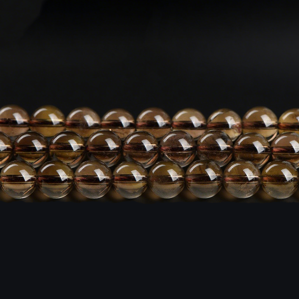 A close-up image showing multiple strands of polished smoky quartz round beads laid out horizontally. The beads display a translucent brown hue with a smooth, glossy surface and visible internal textures.