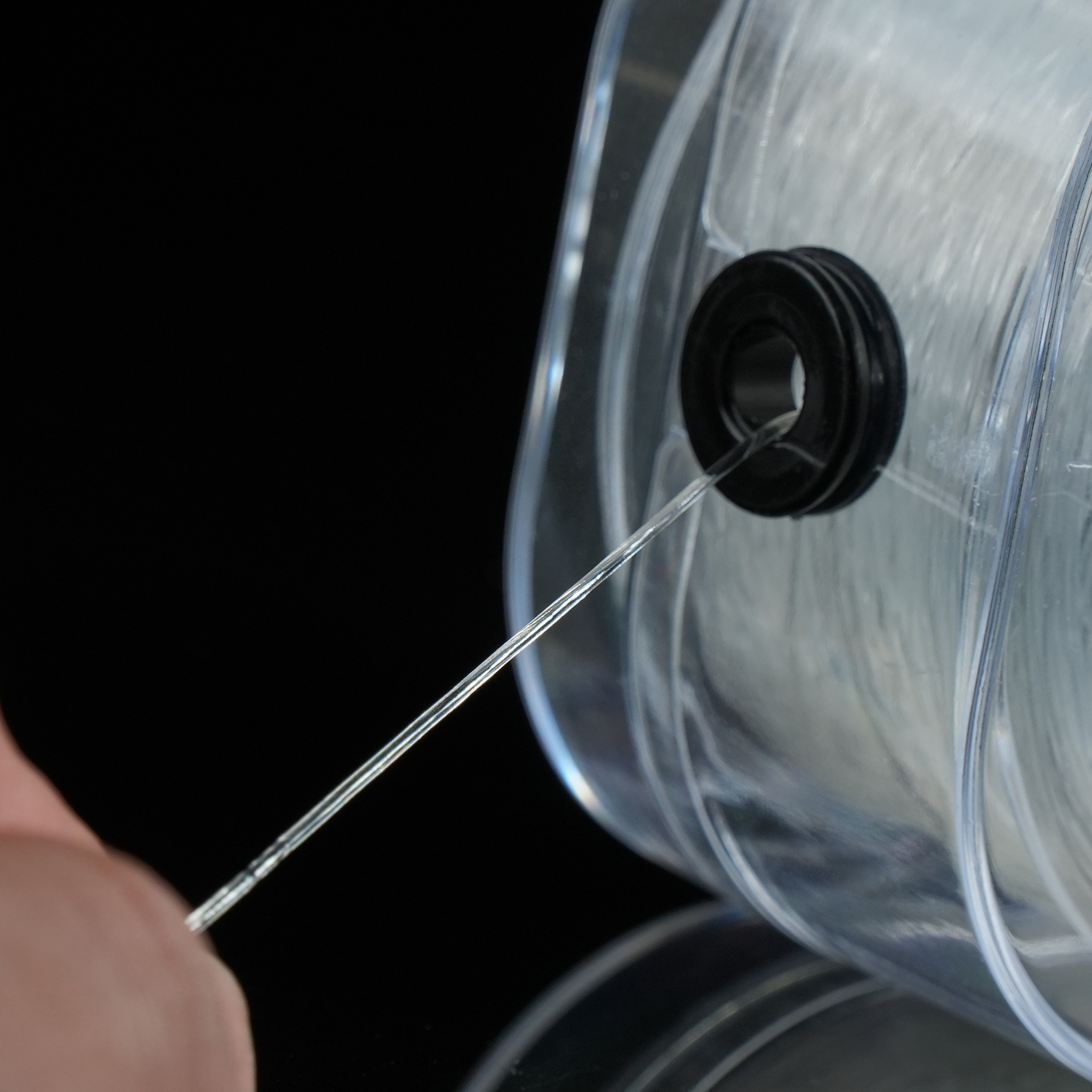 This close-up shot shows a hand gently pulling the elastic thread through a small black guide in the dispenser. The thread is clear and smooth, designed for comfort and ease of use.