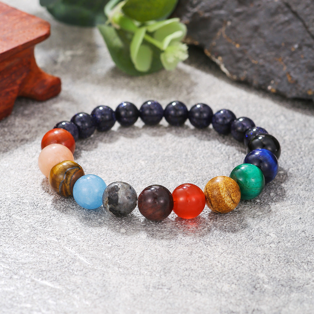 A planetary crystal bracelet placed on a rustic surface with greenery, showcasing polished gemstone beads.