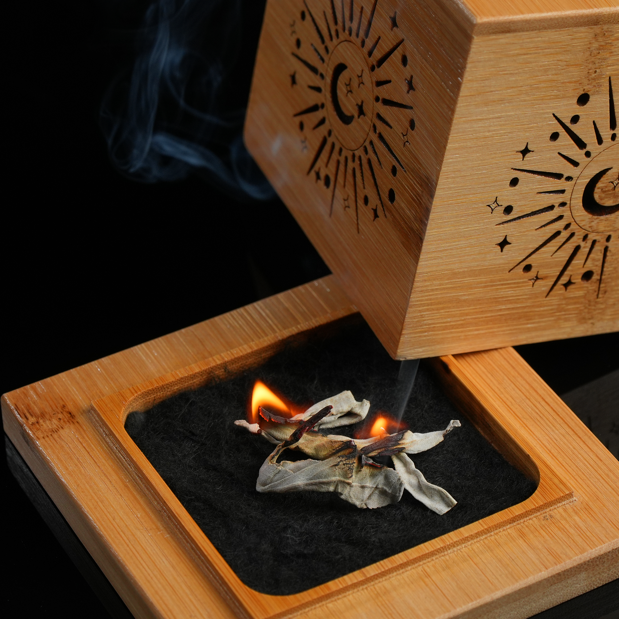 Burning white sage inside an open bamboo smudge tray with etched celestial symbols.