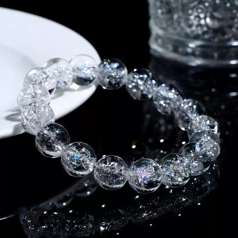 A Himalayan quartz bracelet displayed near a clear cup on a glossy black surface, reflecting vibrant light sparkles.