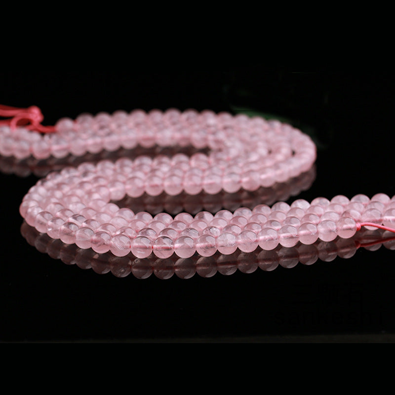 Strands of light pink rose quartz beads are arranged in an elegant curve across a glossy black background. The soft pink thread running through the beads is slightly visible, complementing their natural hue.