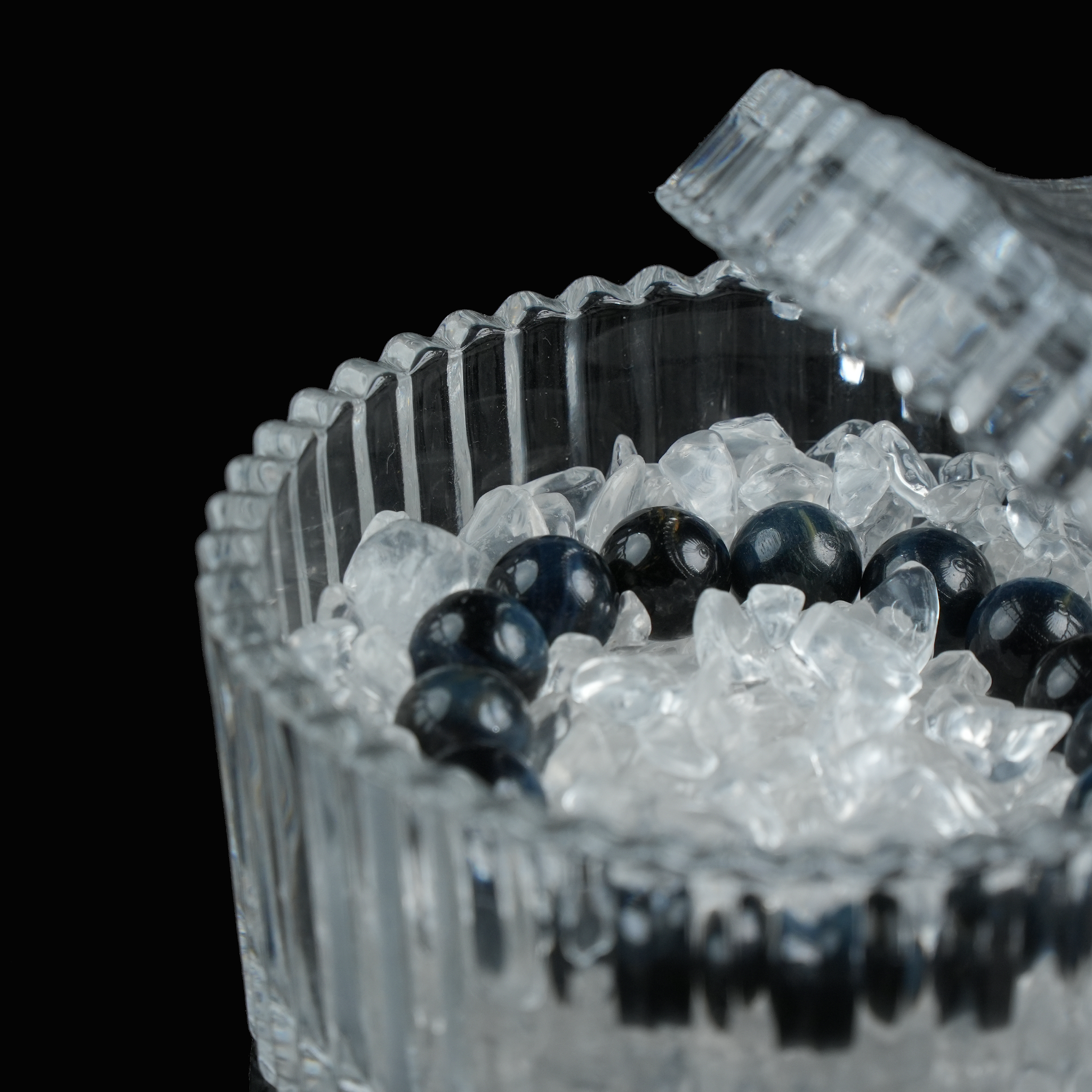 A close-up of a crystal bracelet surrounded by clear quartz chips inside a ridged glass container.