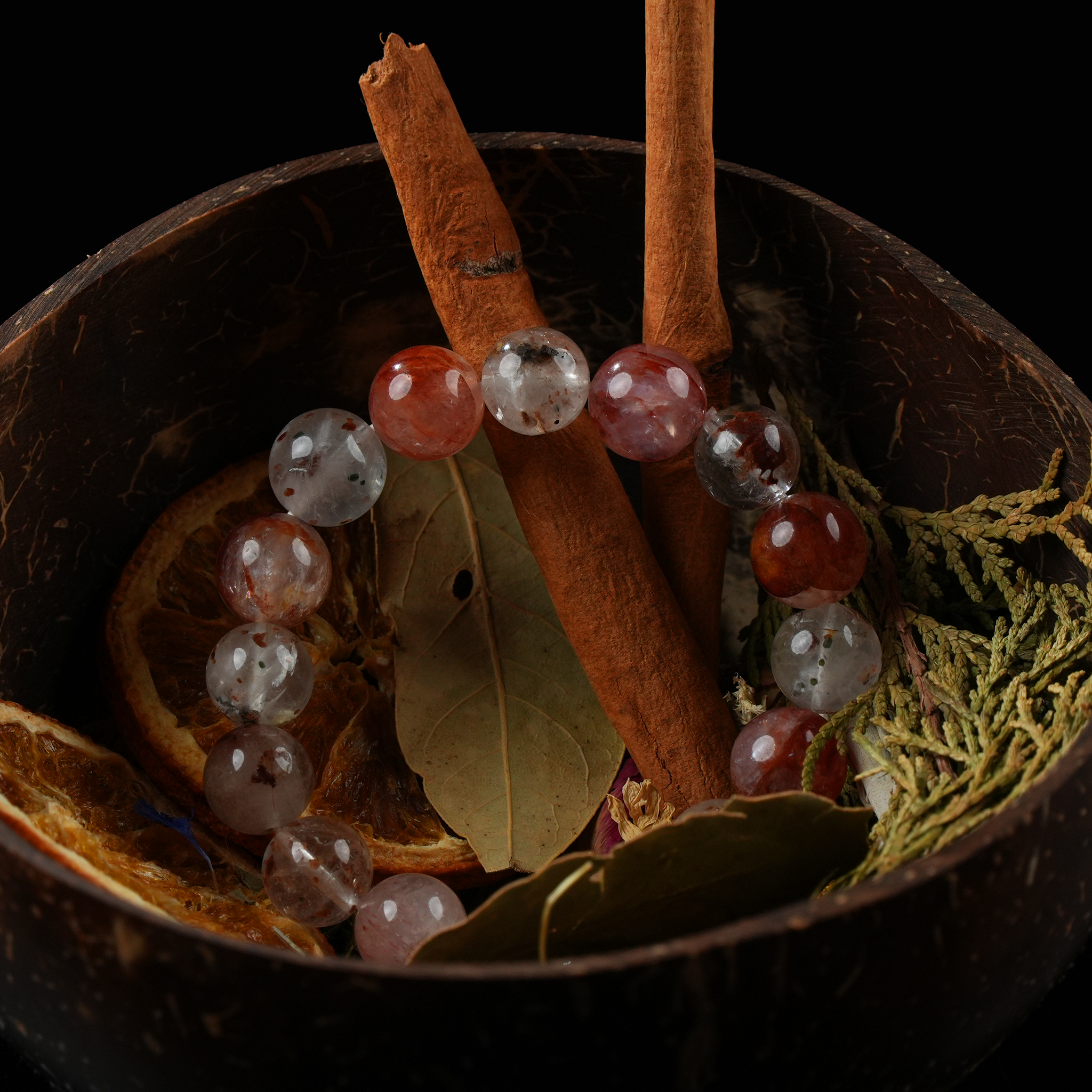 Close-up of a gemstone bracelet with cinnamon and herbs inside a handmade coconut bowl.