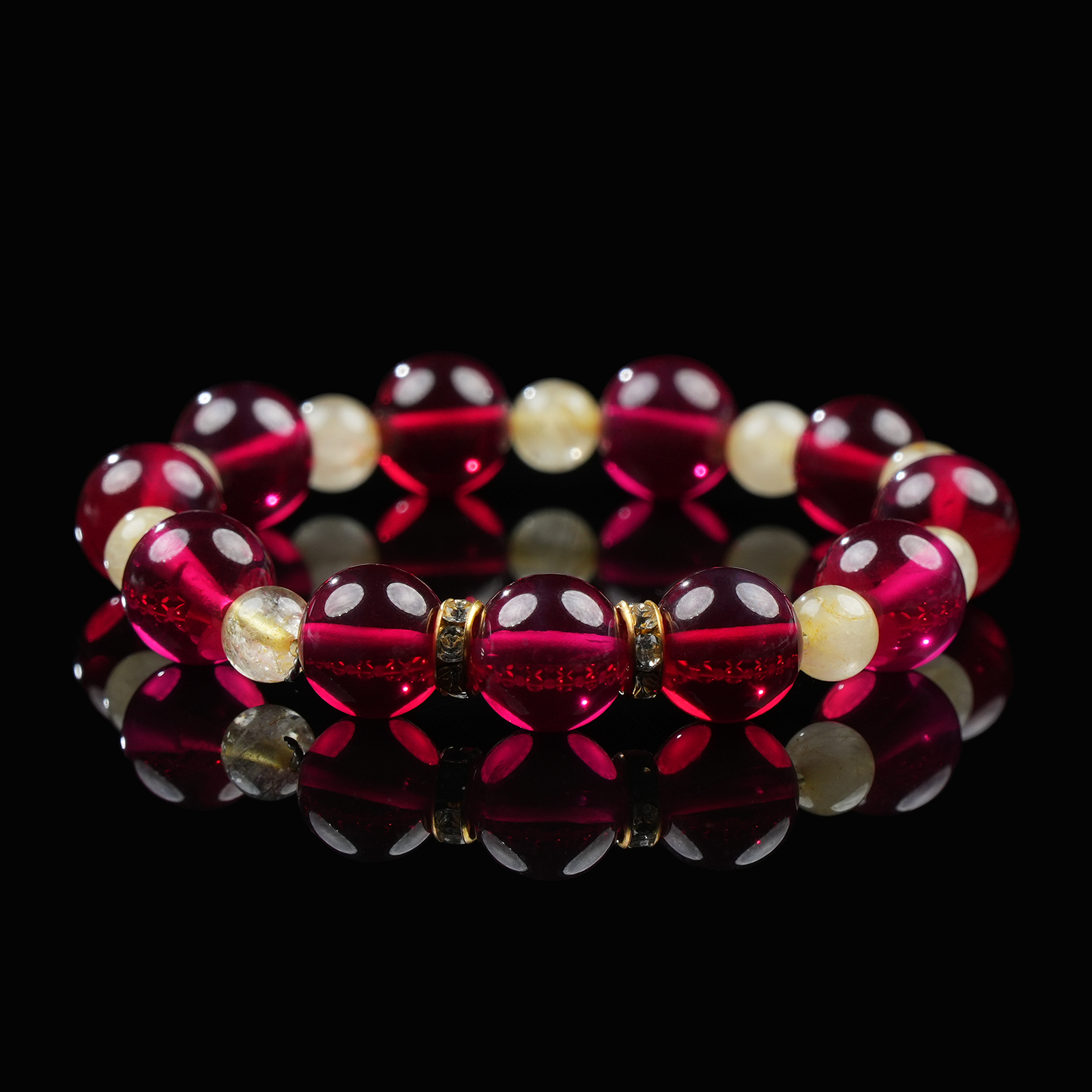 A vibrant bracelet composed of deep red garnet and golden quartz beads, accented with gold-toned spacers, resting elegantly on a glossy black background with mirror reflection.