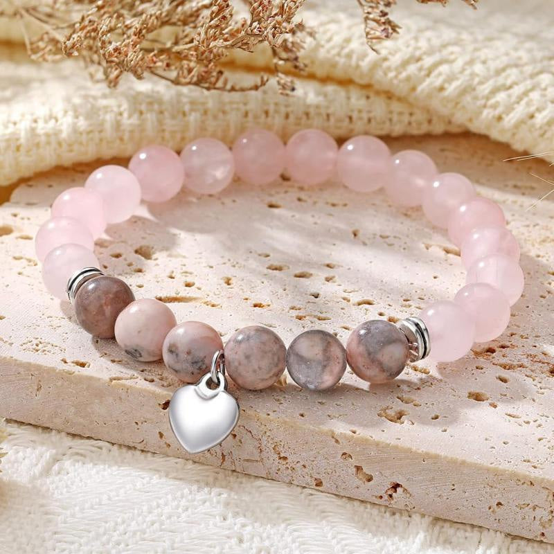 A soft pink bracelet with a heart charm resting on a beige textured fabric, emphasizing comfort and warmth.