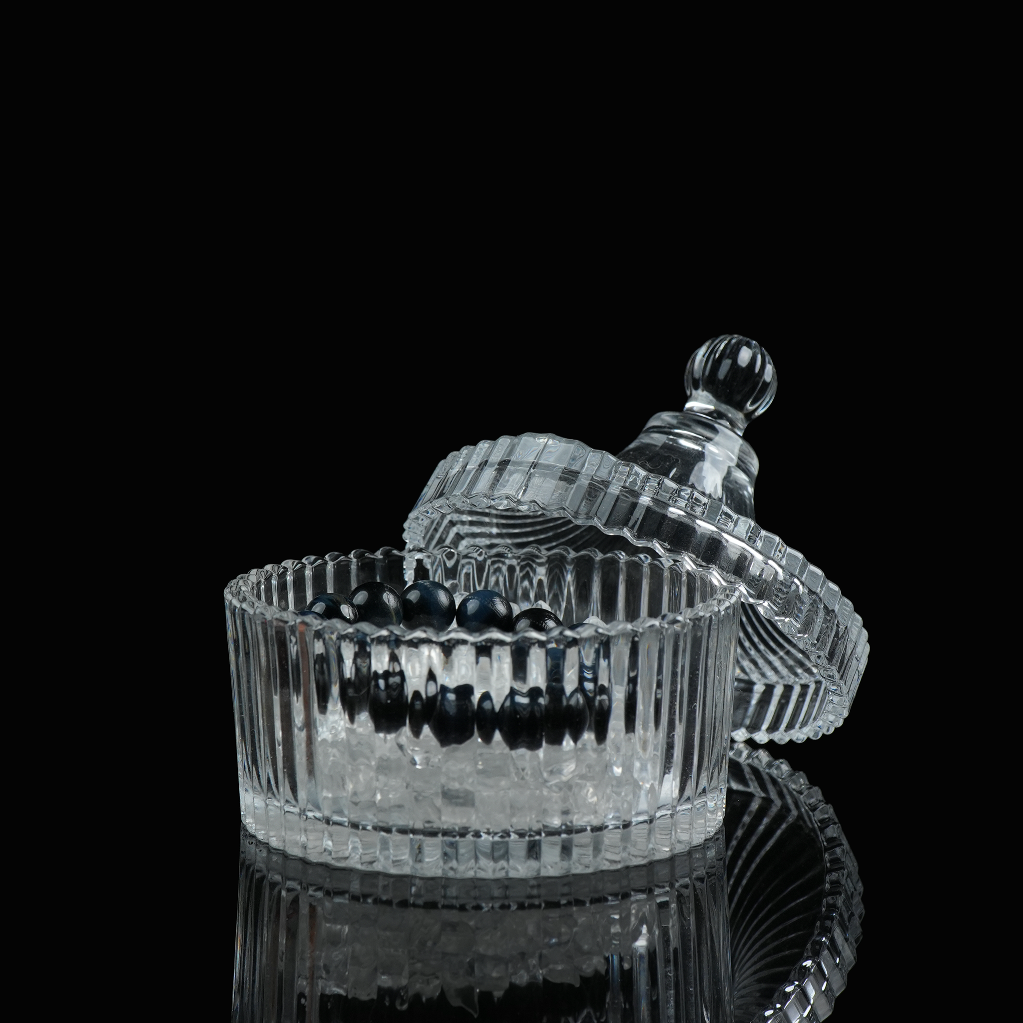 A top-open glass dish with the lid beside it, filled with crystal chips used for spiritual and jewelry cleansing.