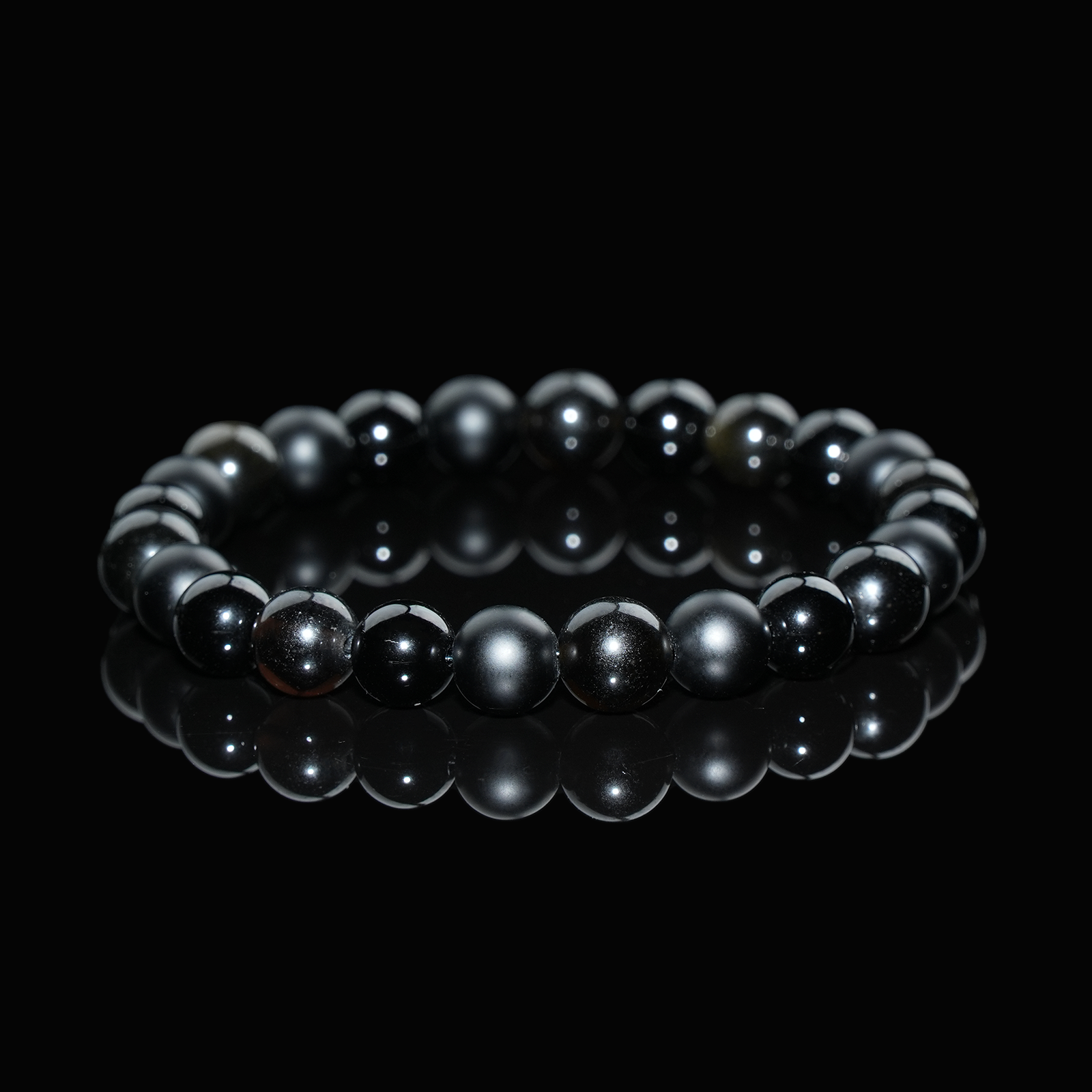 Close-up view of a gold sheen obsidian bracelet featuring polished black beads with subtle golden highlights, displayed on a black reflective background to emphasize its sleek, protective energy.