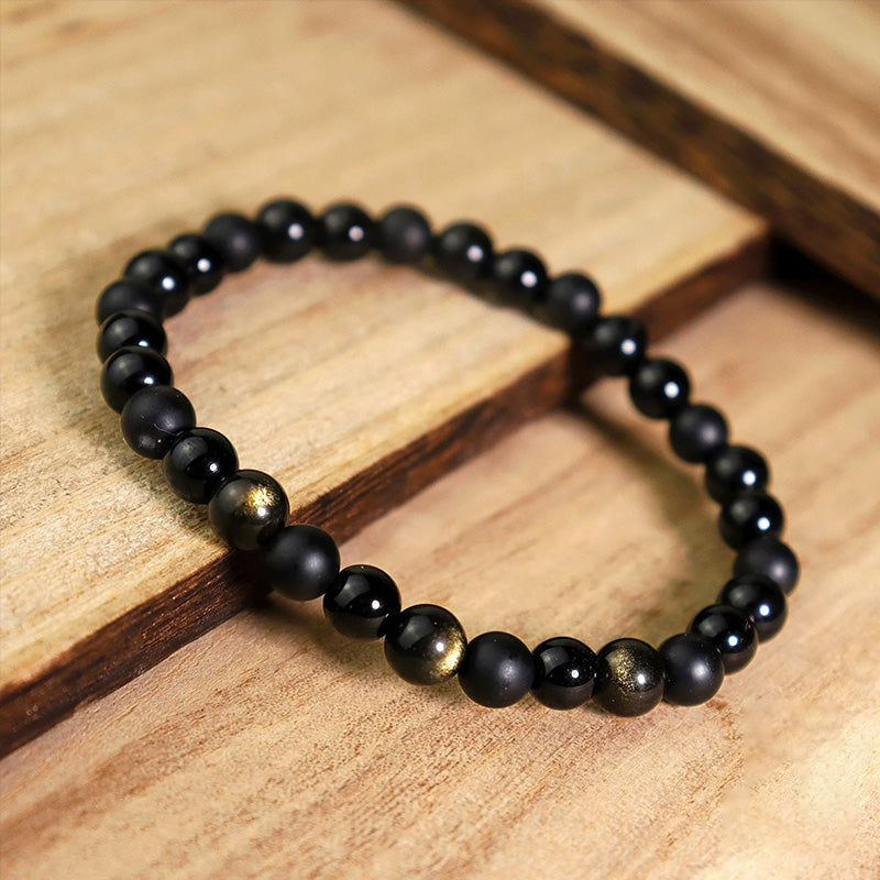 Beaded bracelet placed diagonally on wooden steps, highlighting the contrast between smooth black and golden shimmer stones for a sense of calm power.