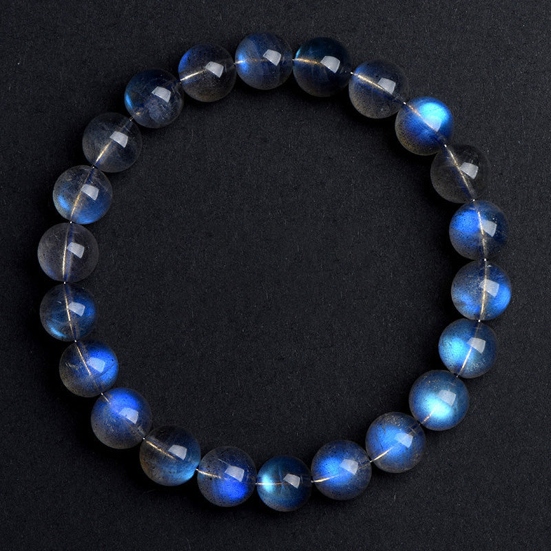 High-resolution top-down shot of a gray moonstone bracelet on a dark surface, where vibrant blue reflections dance across the translucent gray beads.