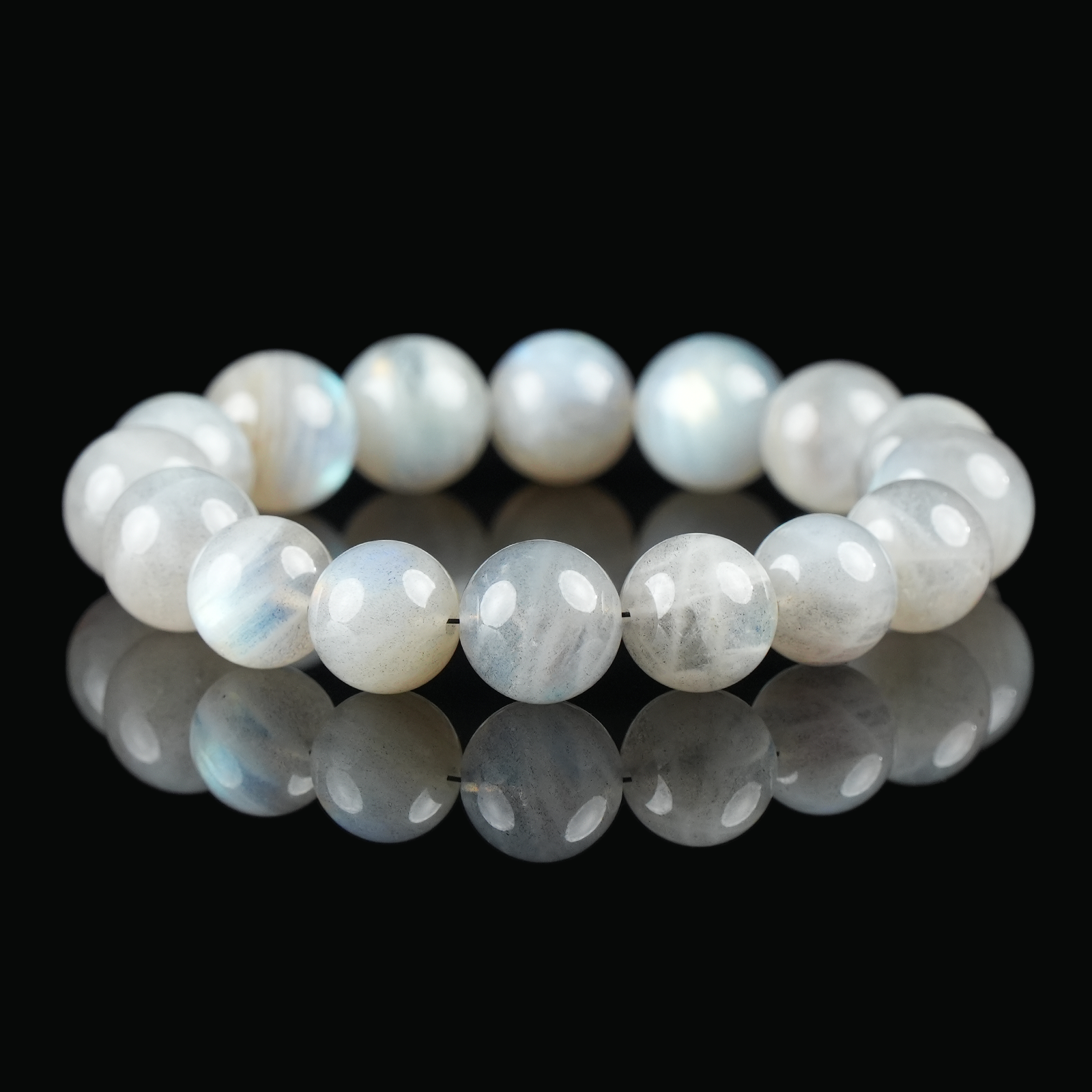 Flat lay of gray moonstone bracelet with round beads showing soft bluish sheen on black reflective background – used for calming energy.