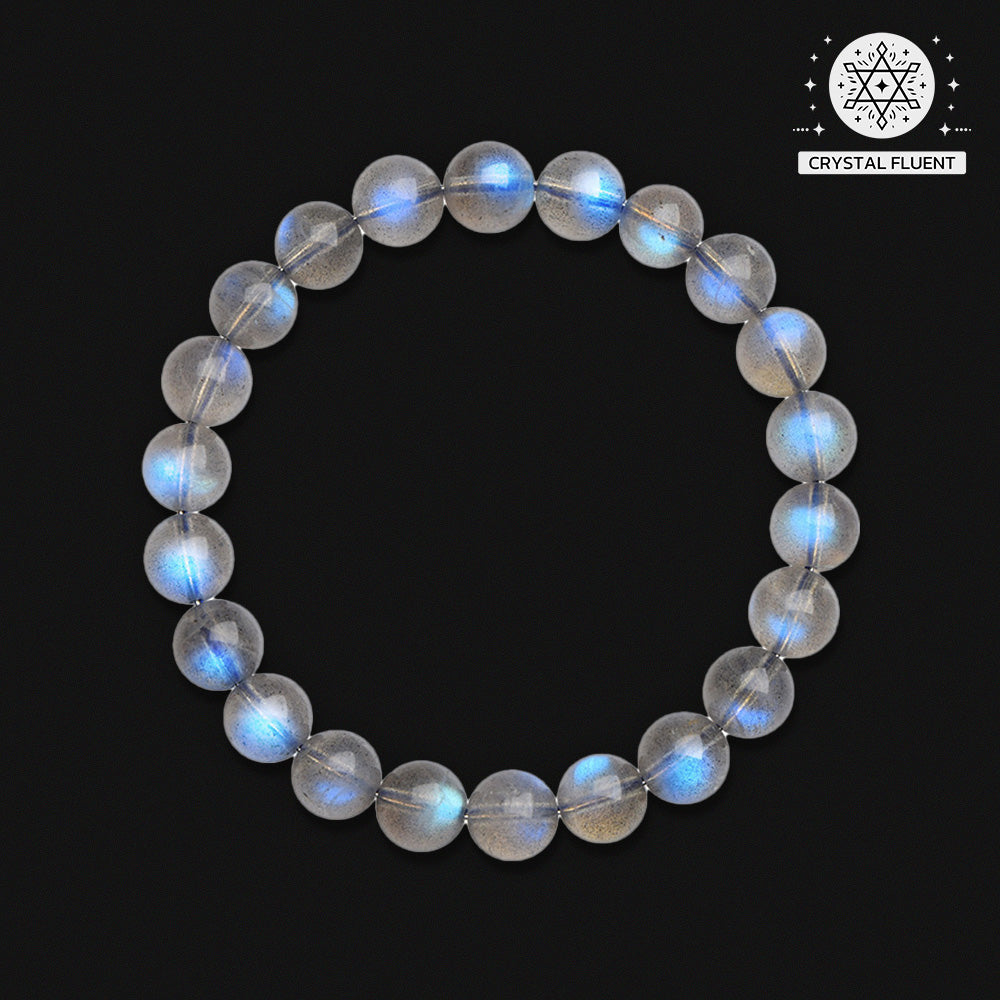 Circular arrangement of a gray moonstone bracelet photographed from above on a matte black background, showcasing the stone’s inner glow and natural inclusions.