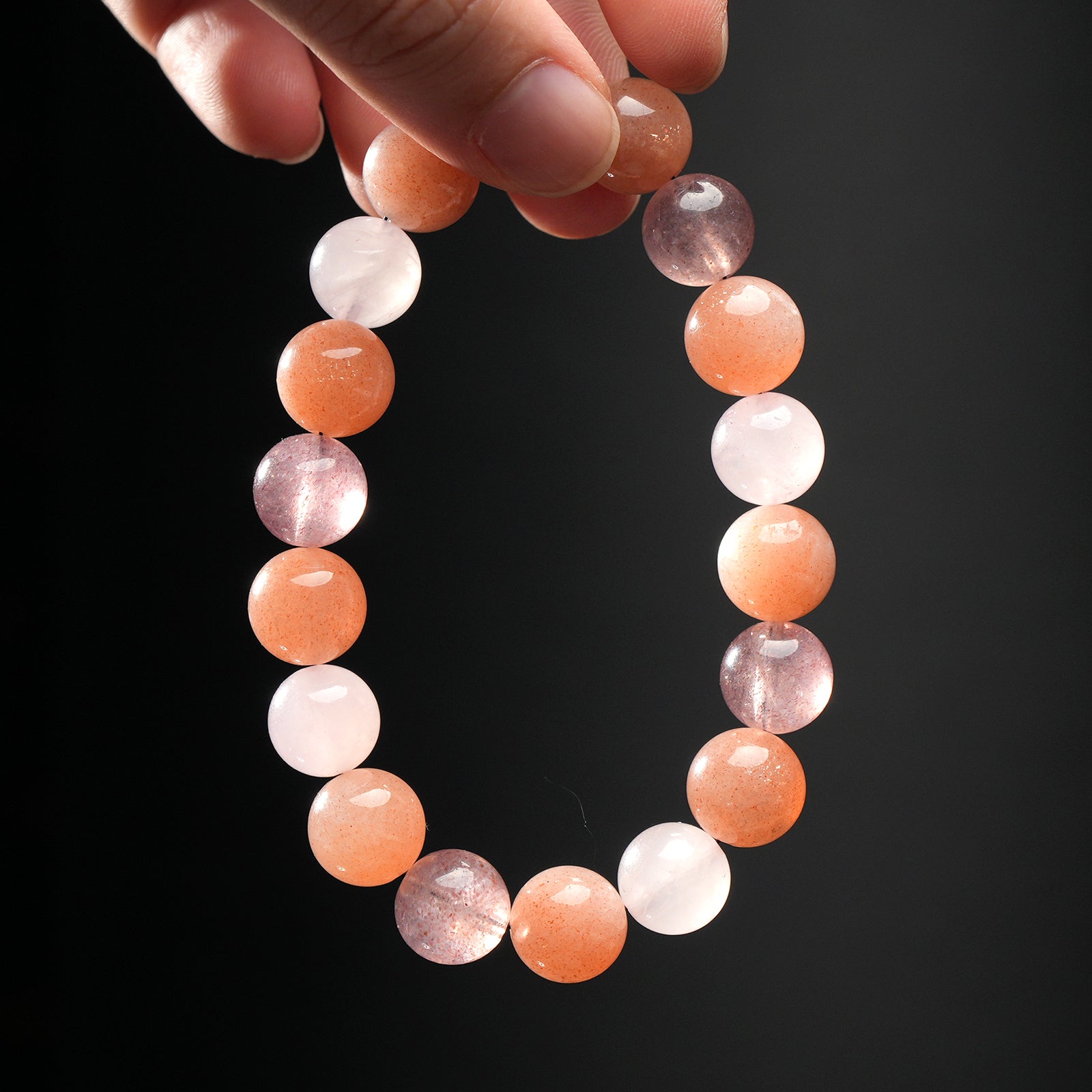 Close-up of hand holding Cancer zodiac crystal bracelet made with calming moonstone, nurturing strawberry quartz, and energizing sunstone.