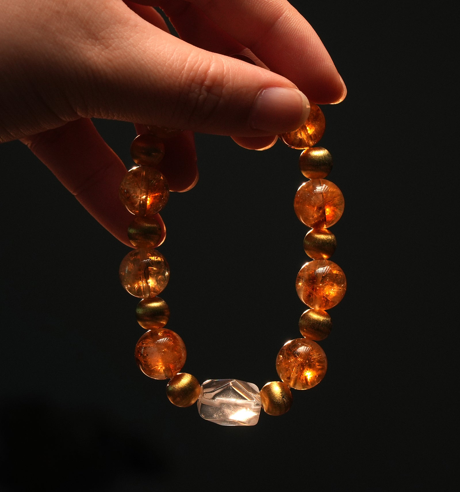 A hand holding citrine crystal bracelet with gold-toned spacers and transparent centerpiece, symbolizing positivity and manifestation power.