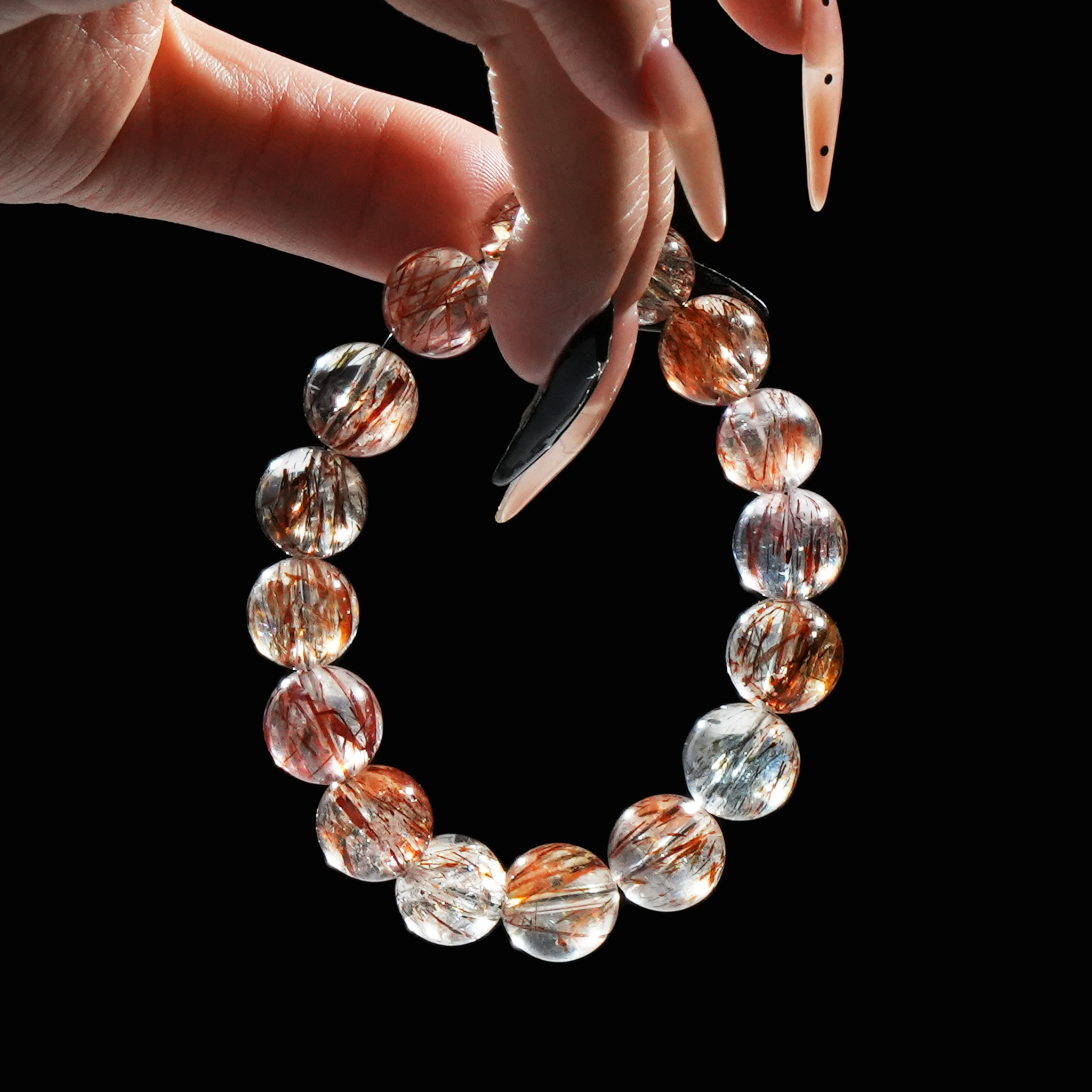 Hand holding red rutilated quartz bracelet, showing the clarity and deep red rutile inclusions in each bead.