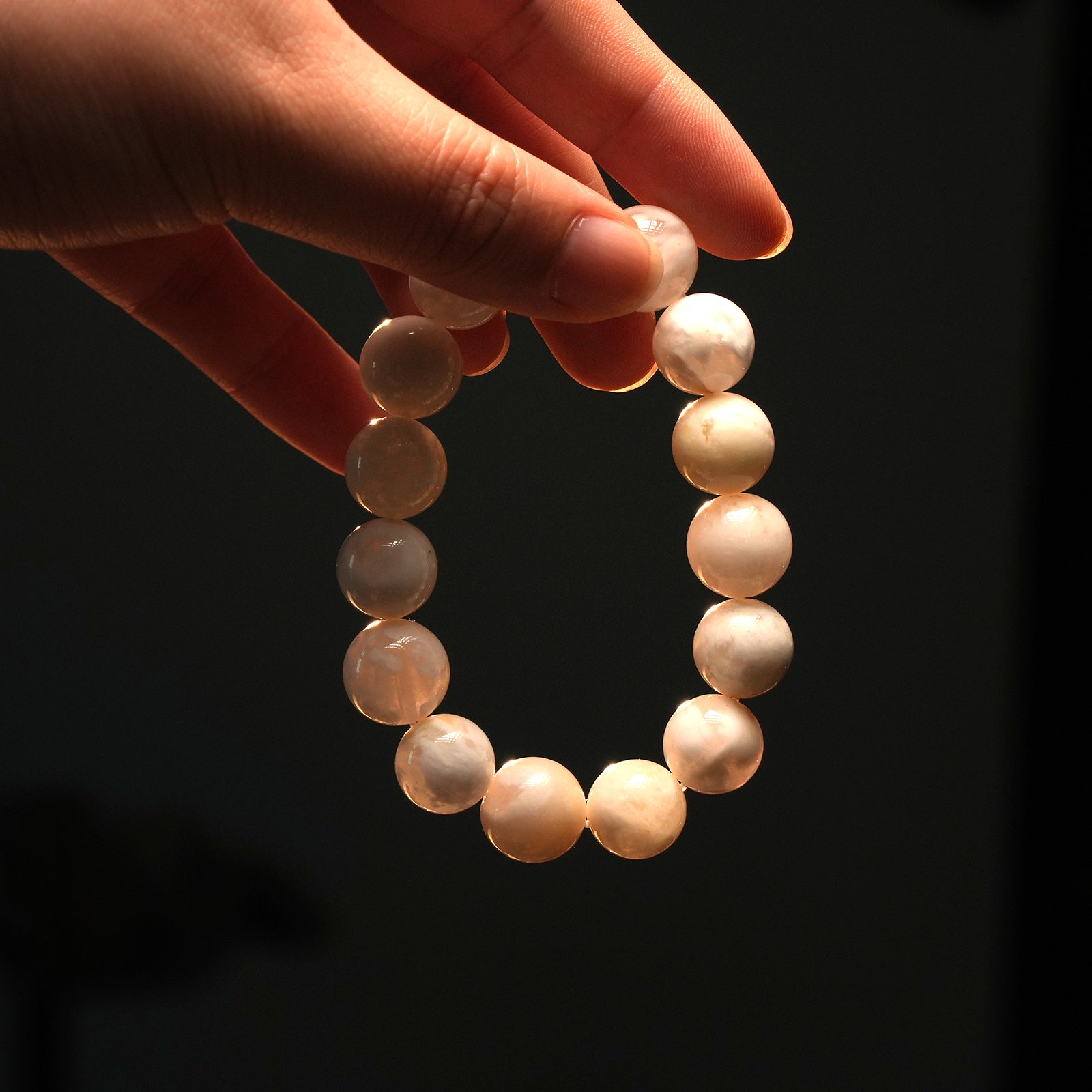 A hand holding snow phantom bracelet in moody lighting, showcasing the ethereal white stones ideal for meditation, healing, and inner clarity.