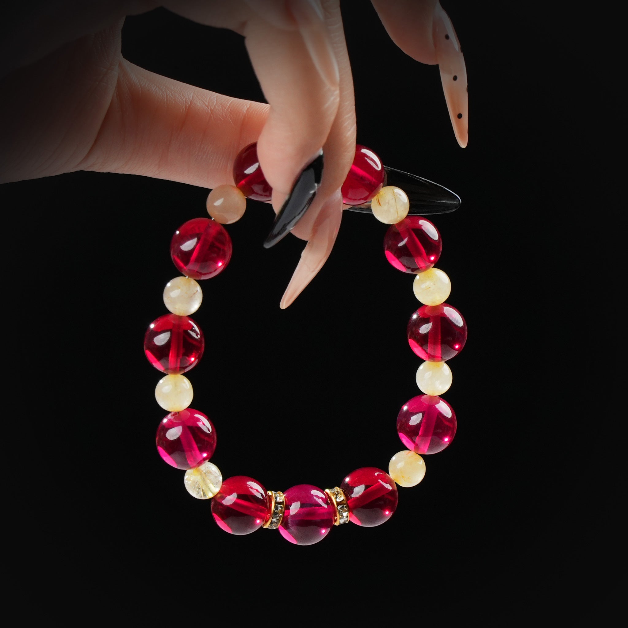 A close-up of a manicured hand delicately holding a garnet and golden quartz bracelet, highlighting the bright red and creamy golden hues of the beads.
