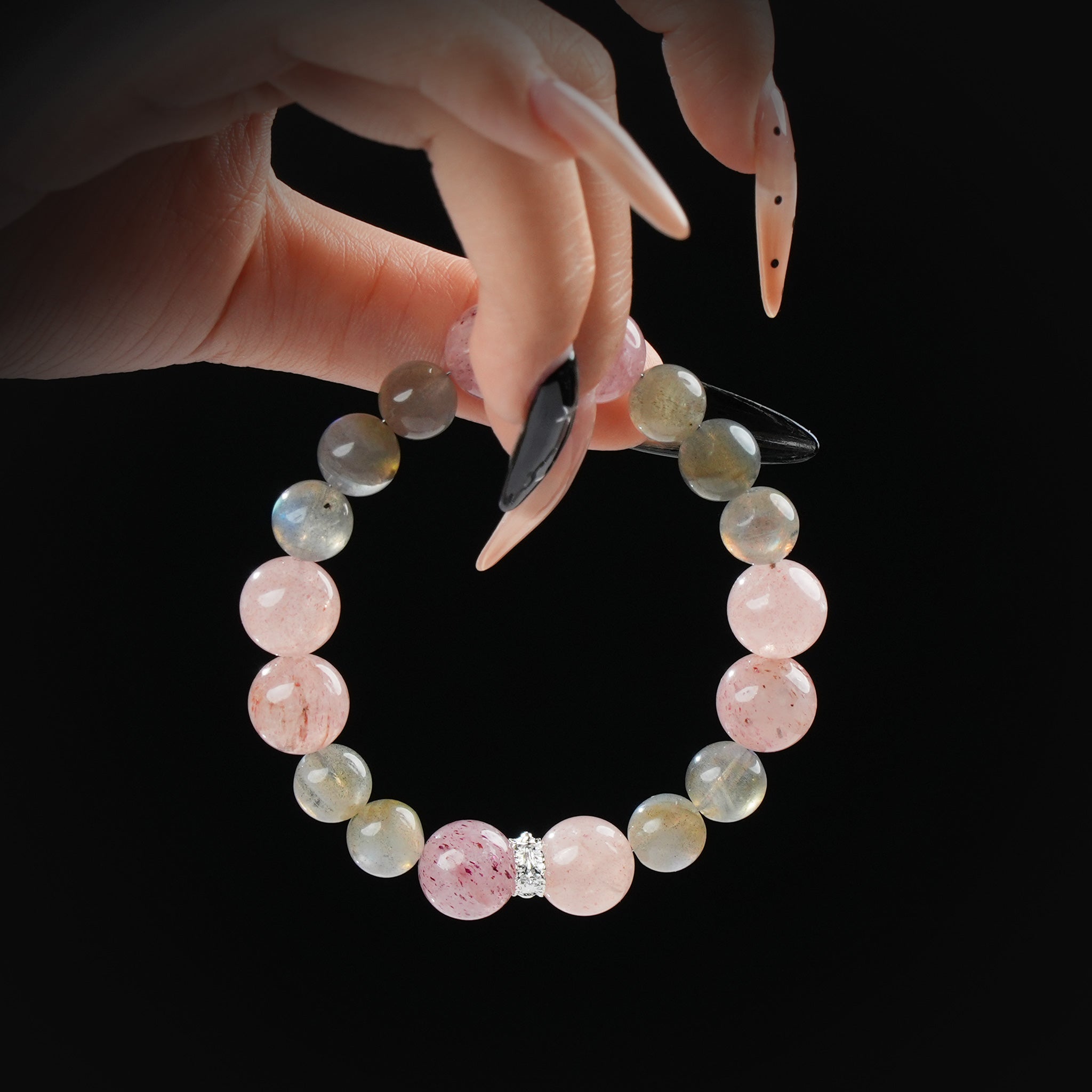 A close-up of a hand delicately holding a natural stone bracelet made of pink strawberry quartz and gray moonstone beads, showing sparkle and color contrast.