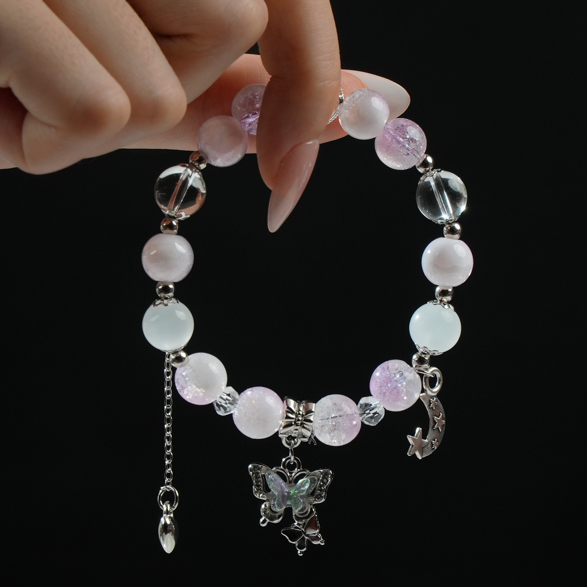 A hand gently holding a pink-to-purple gradient energy bead bracelet, adorned with butterfly and moon charms—light, playful, and full of feminine charm.