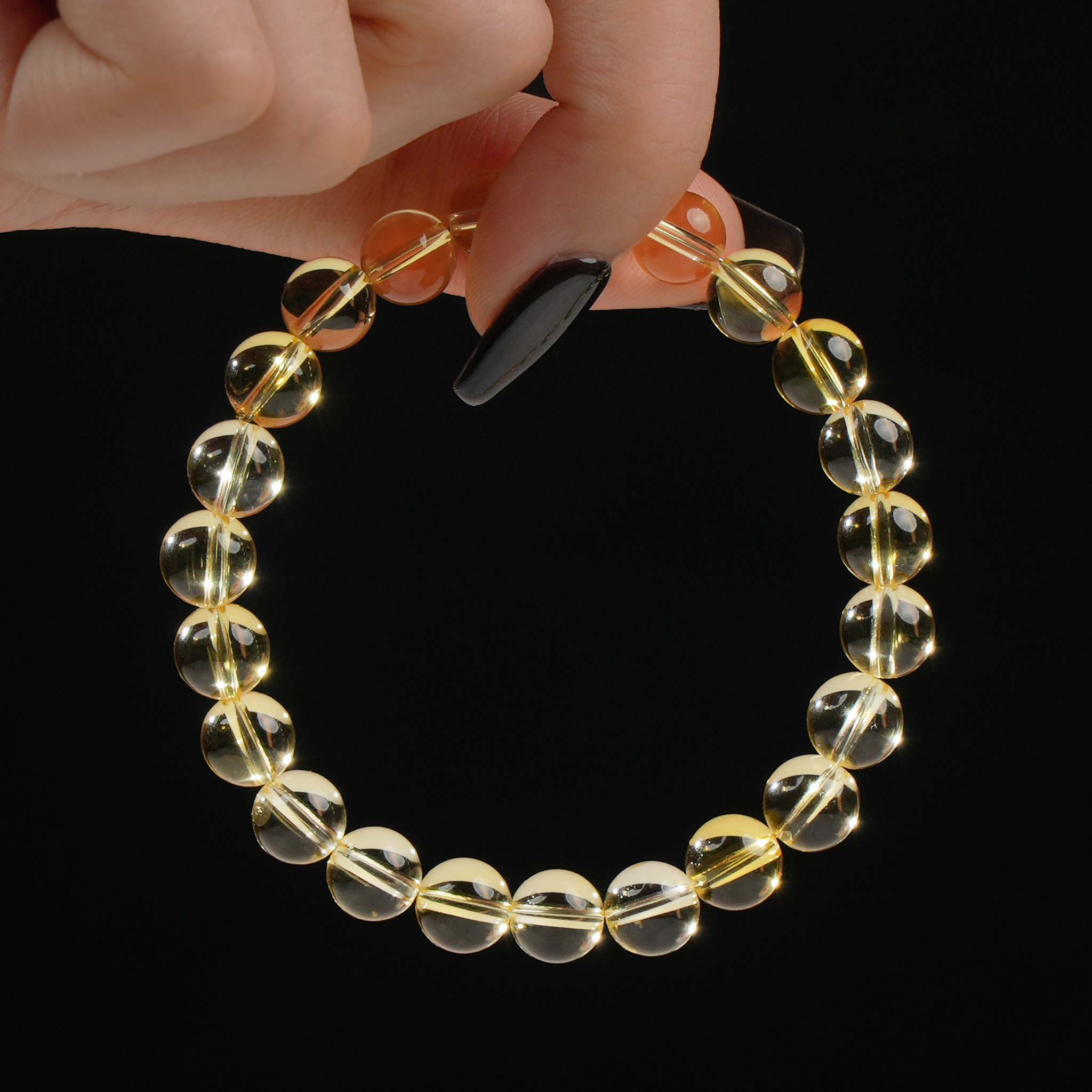 A delicate Citrine bracelet featuring uniform, polished round beads that radiate a golden-yellow hue. The bracelet is held by hand against a dark background, emphasizing the stone’s clarity and luminous glow.