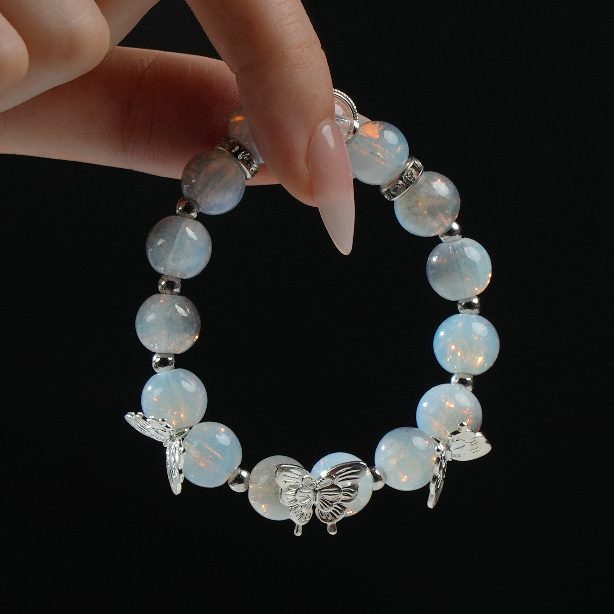 Close-up of a hand holding a luminous opalite butterfly charm bracelet, highlighting the spiritual clarity and celestial sparkle of the ethereal energy beads.