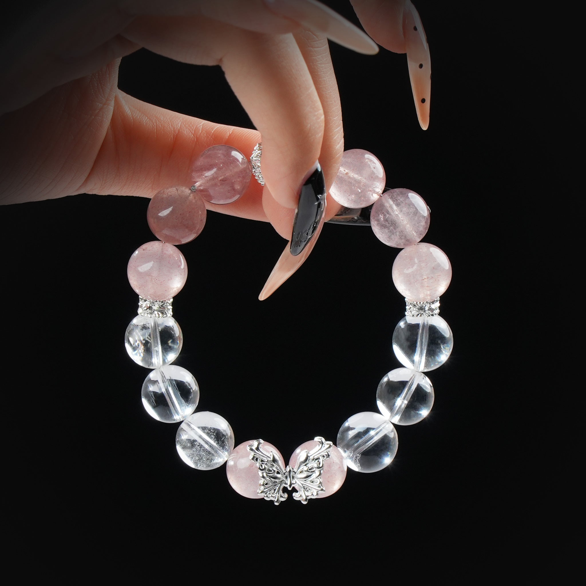 Close-up of a pink and clear crystal bead bracelet featuring a detailed silver butterfly charm, held gently by hand.