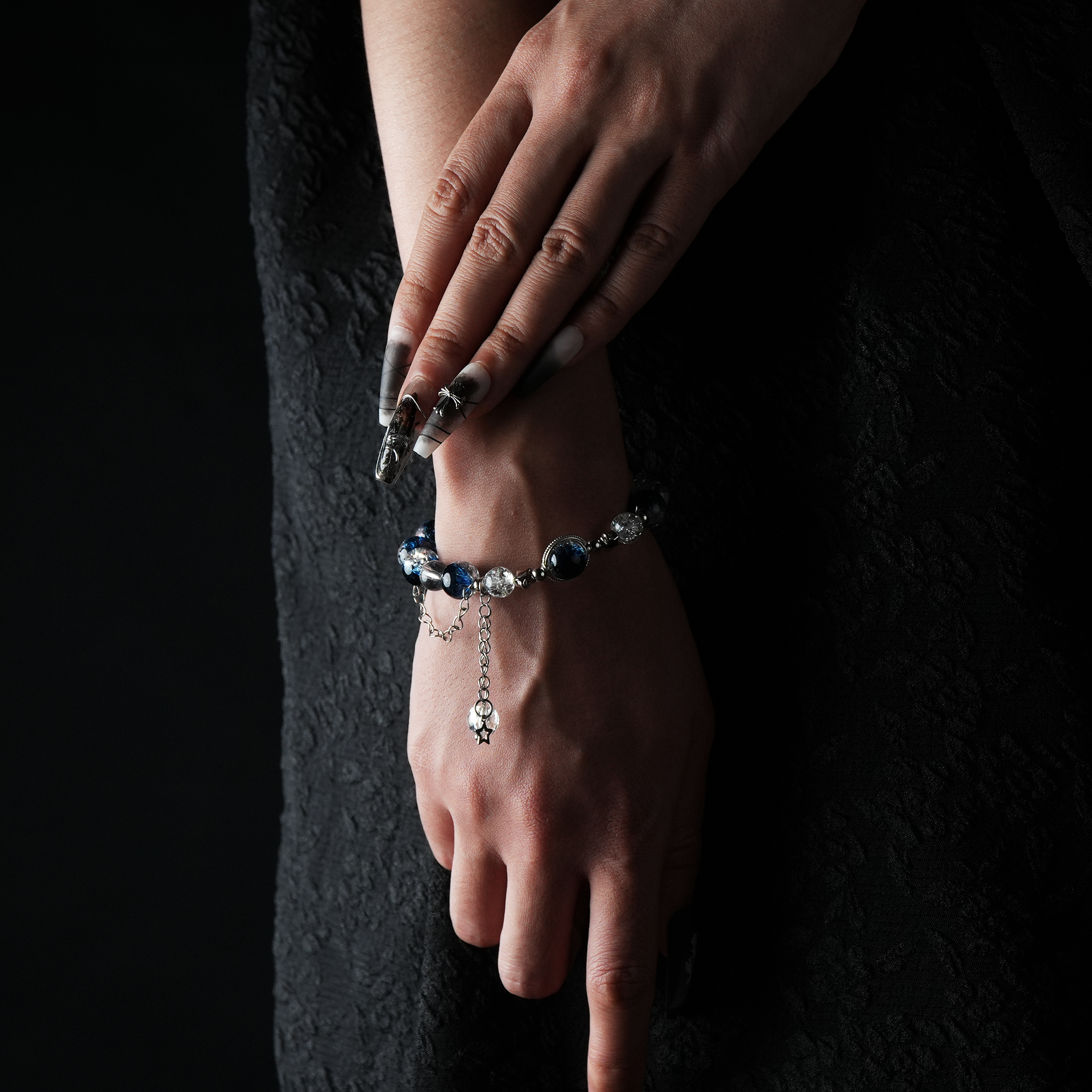 A deep blue crystal bracelet with silver beads and a dangling star charm, worn on the wrist against a black outfit.
