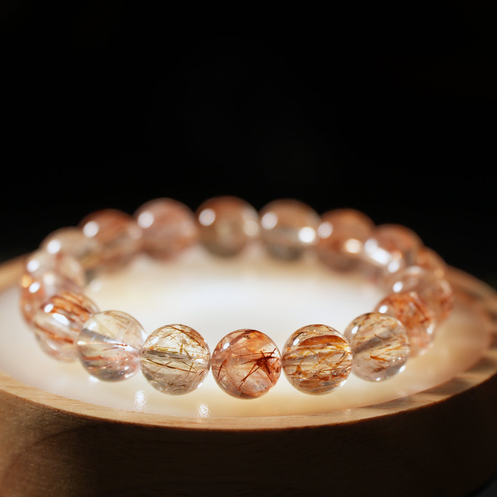 Top-down view of red rutilated quartz bracelet resting on light wood surface, reflecting warm golden-red light.