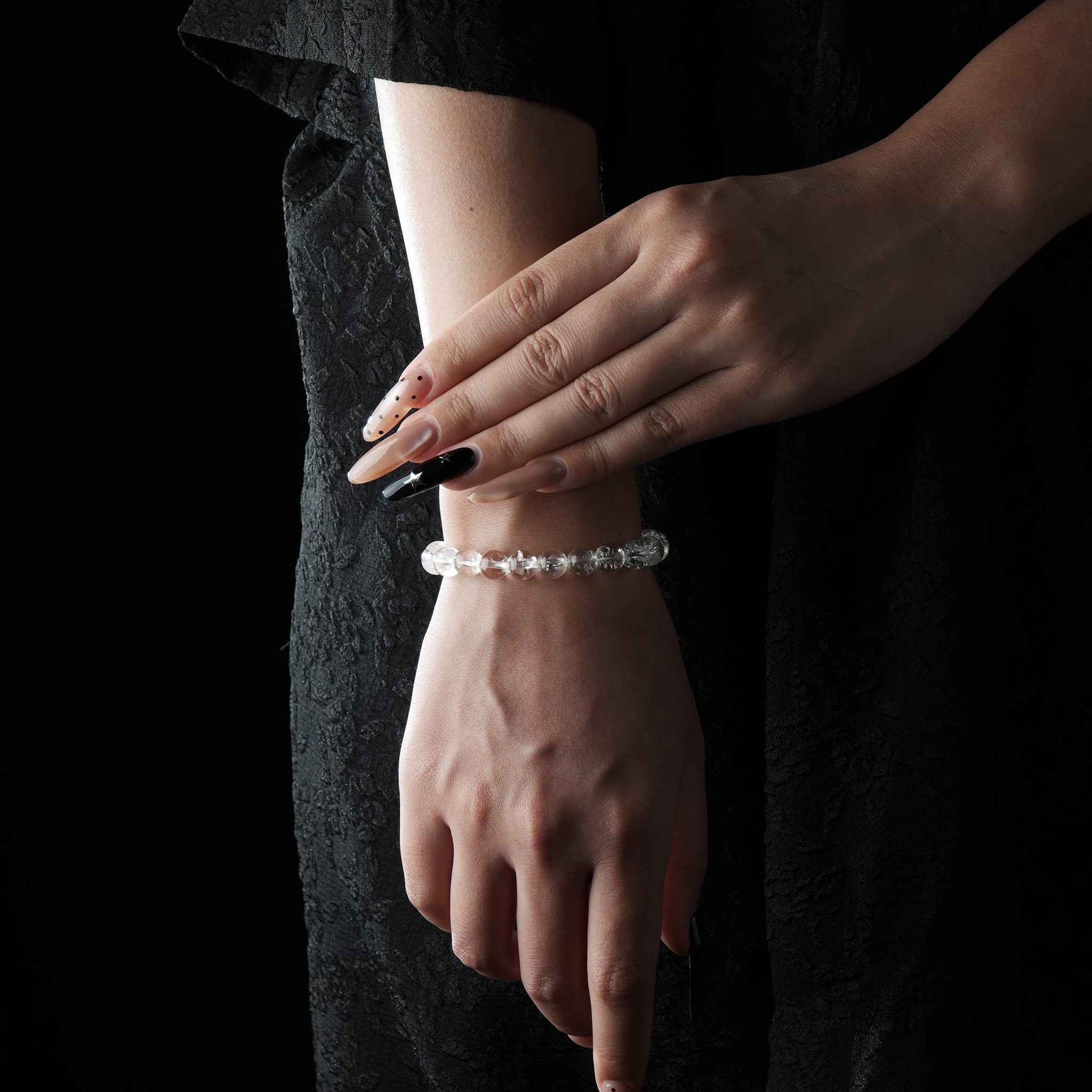 A delicate bracelet made of Himalayan clear quartz beads, worn on the wrist with a black dress background.