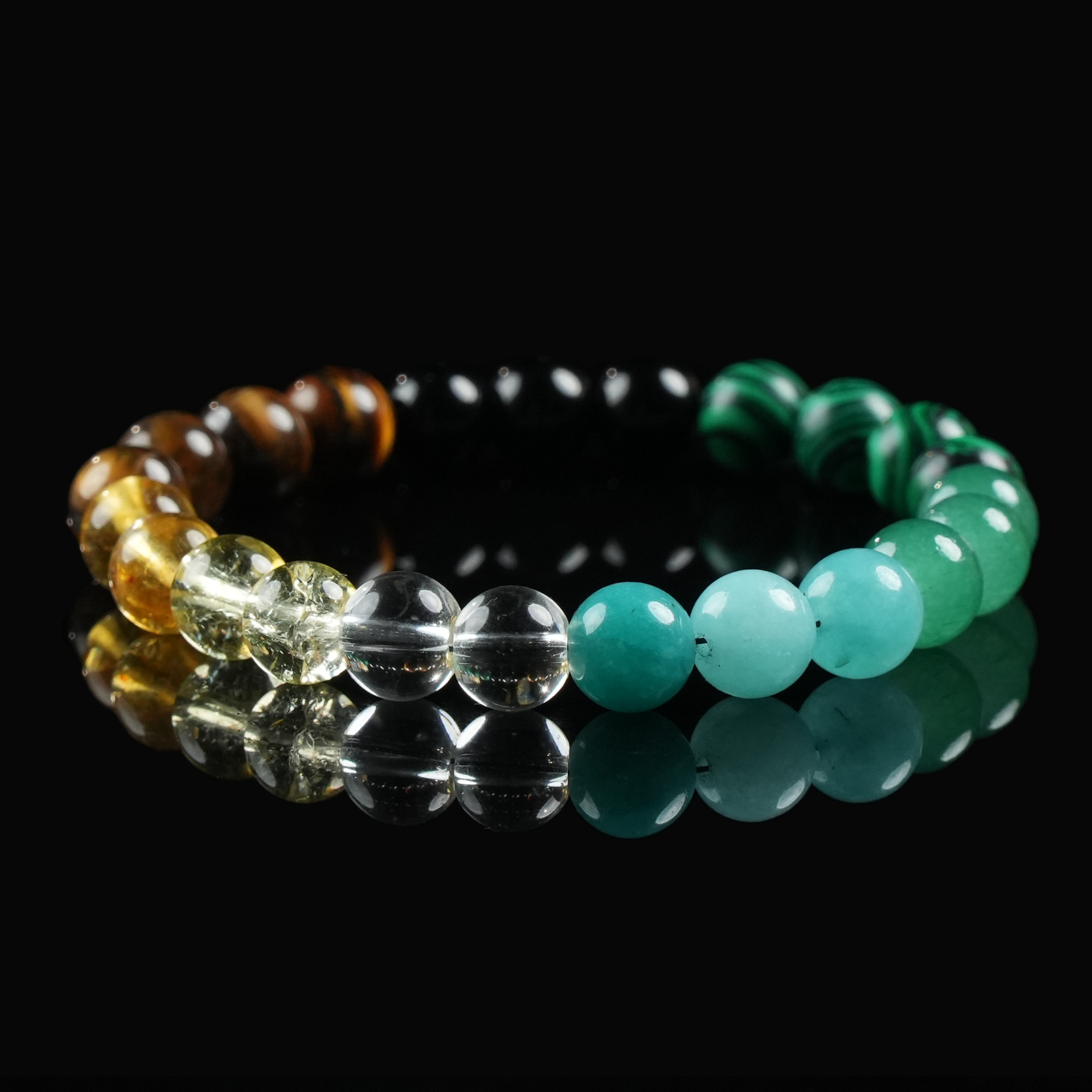 A beaded crystal bracelet with alternating yellow citrine, clear quartz, obsidian, and green jade beads, placed on a reflective black background.