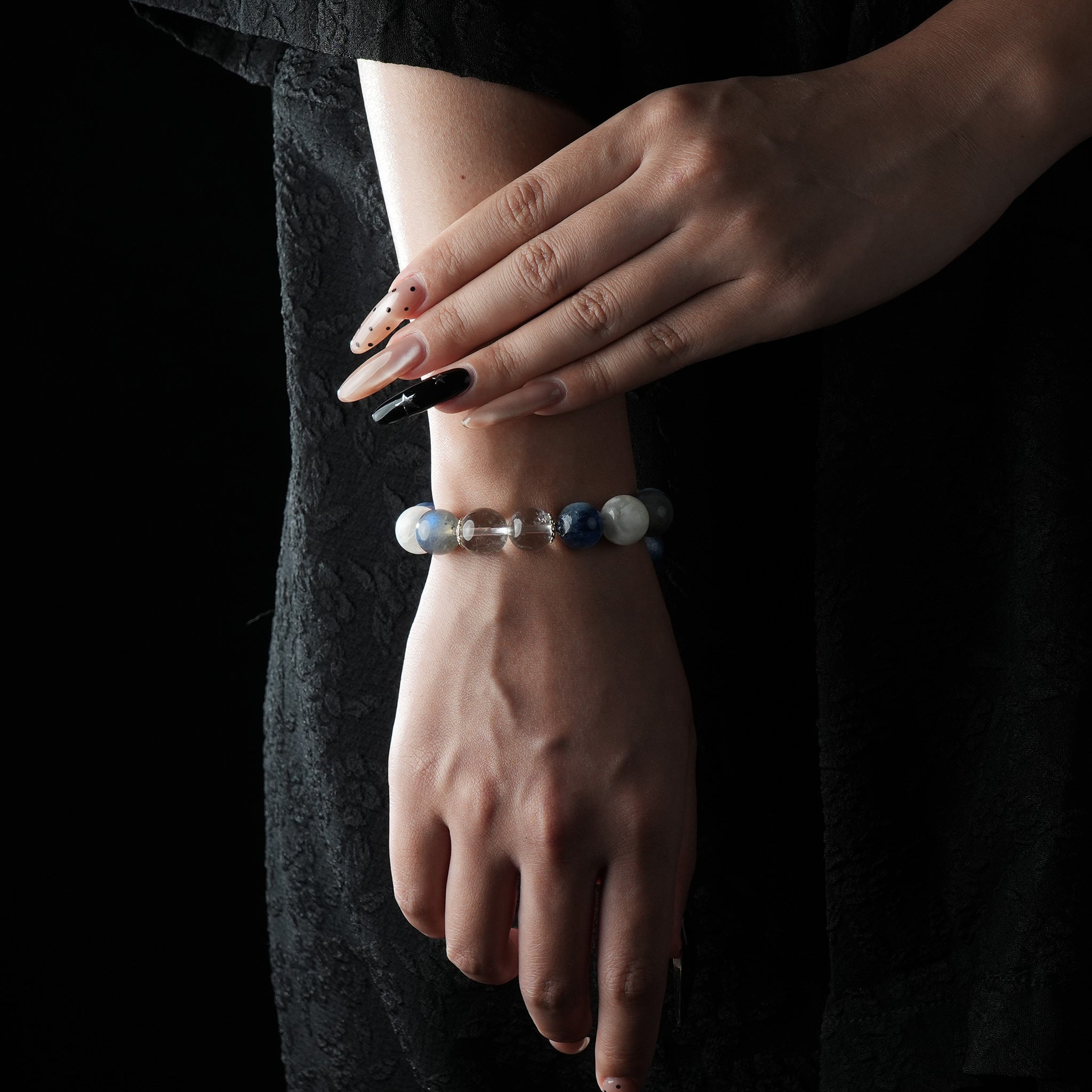 A bracelet made of moonstone, kyanite, and snowflake ghost quartz, shown on a wrist against a dark outfit.