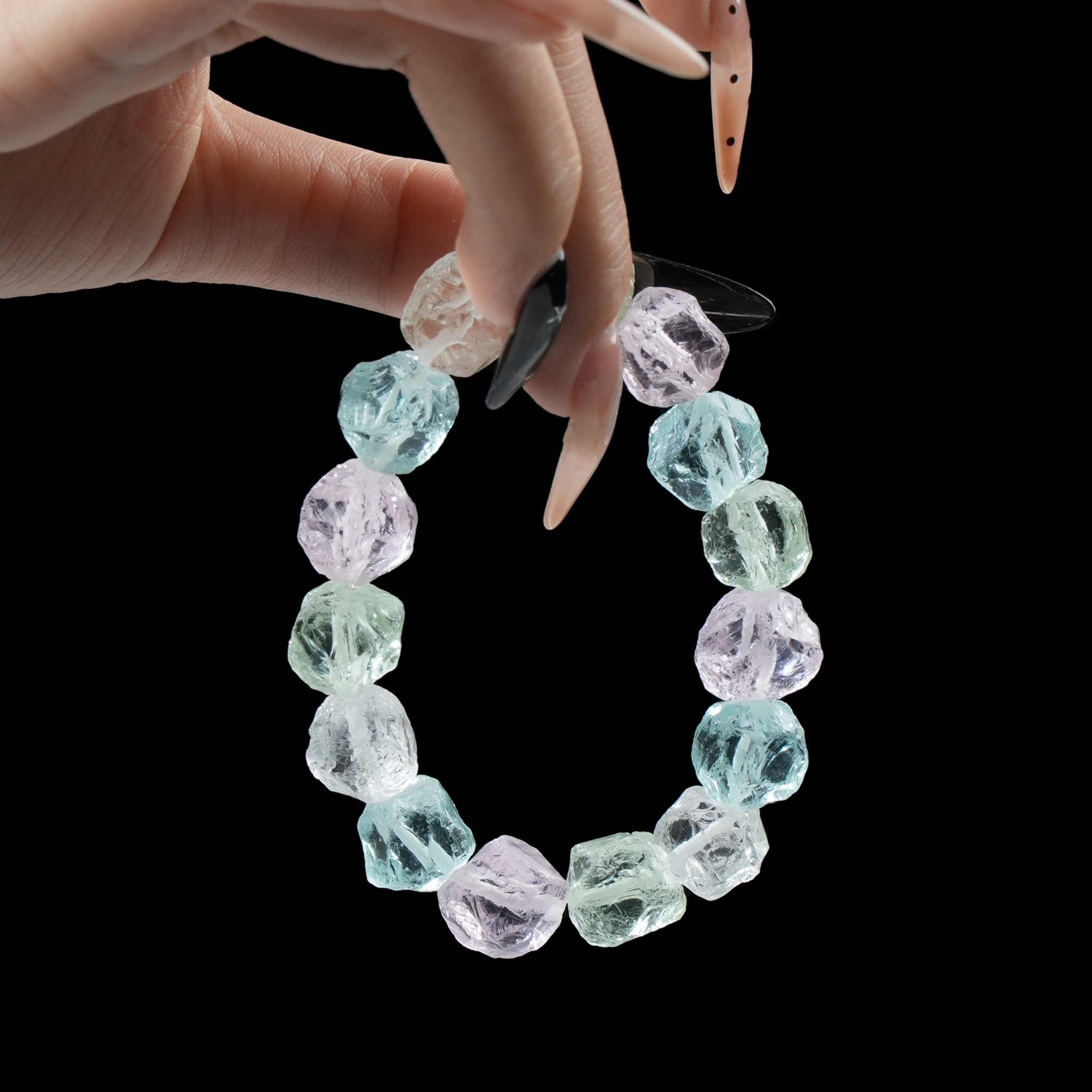 A hand holding the natural raw crystal bracelet, showcasing its unique rough texture and vibrant colors against a dark background.
