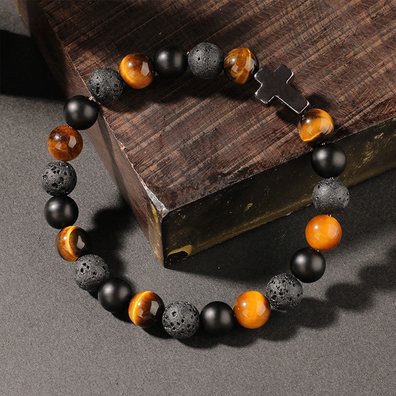 Angled view of a bracelet made with earthy stones and cross detail, styled on wood to reflect strength, elemental balance, and protective energy.