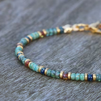 A detailed view of small turquoise and multicolor disc beads strung into an anklet with gold findings.